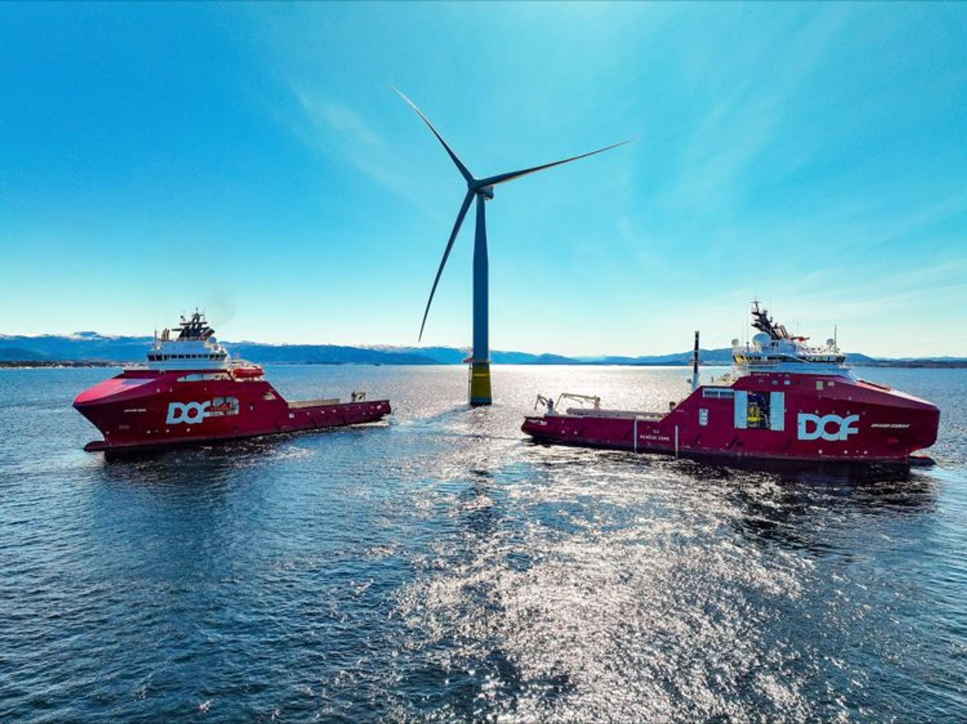 Two red boats in front of an offshore wind turbine