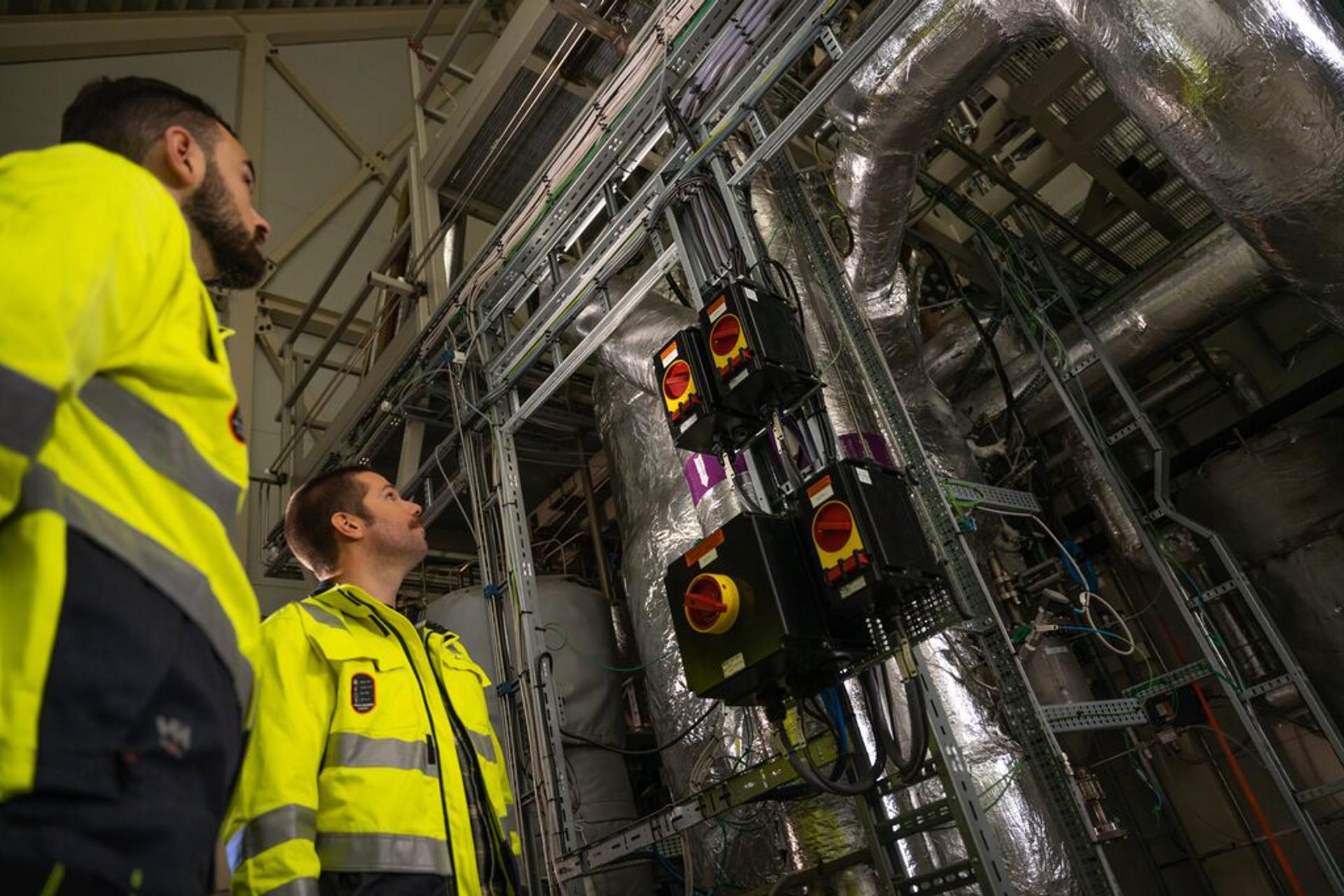 Two workers in yellow jackets inspecting a hydrogen plant