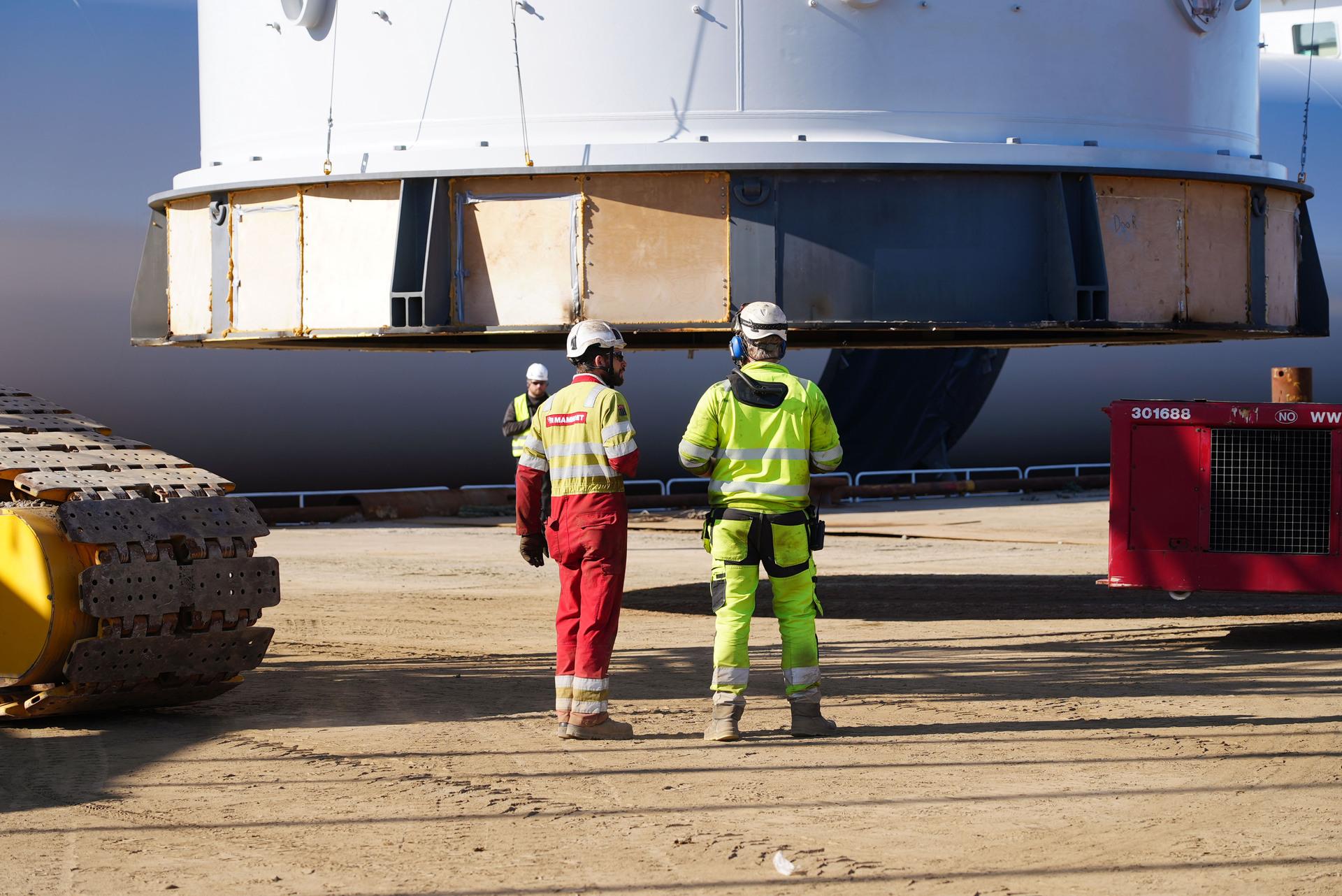 Three workers standing near a floating offshore wind turbine on land