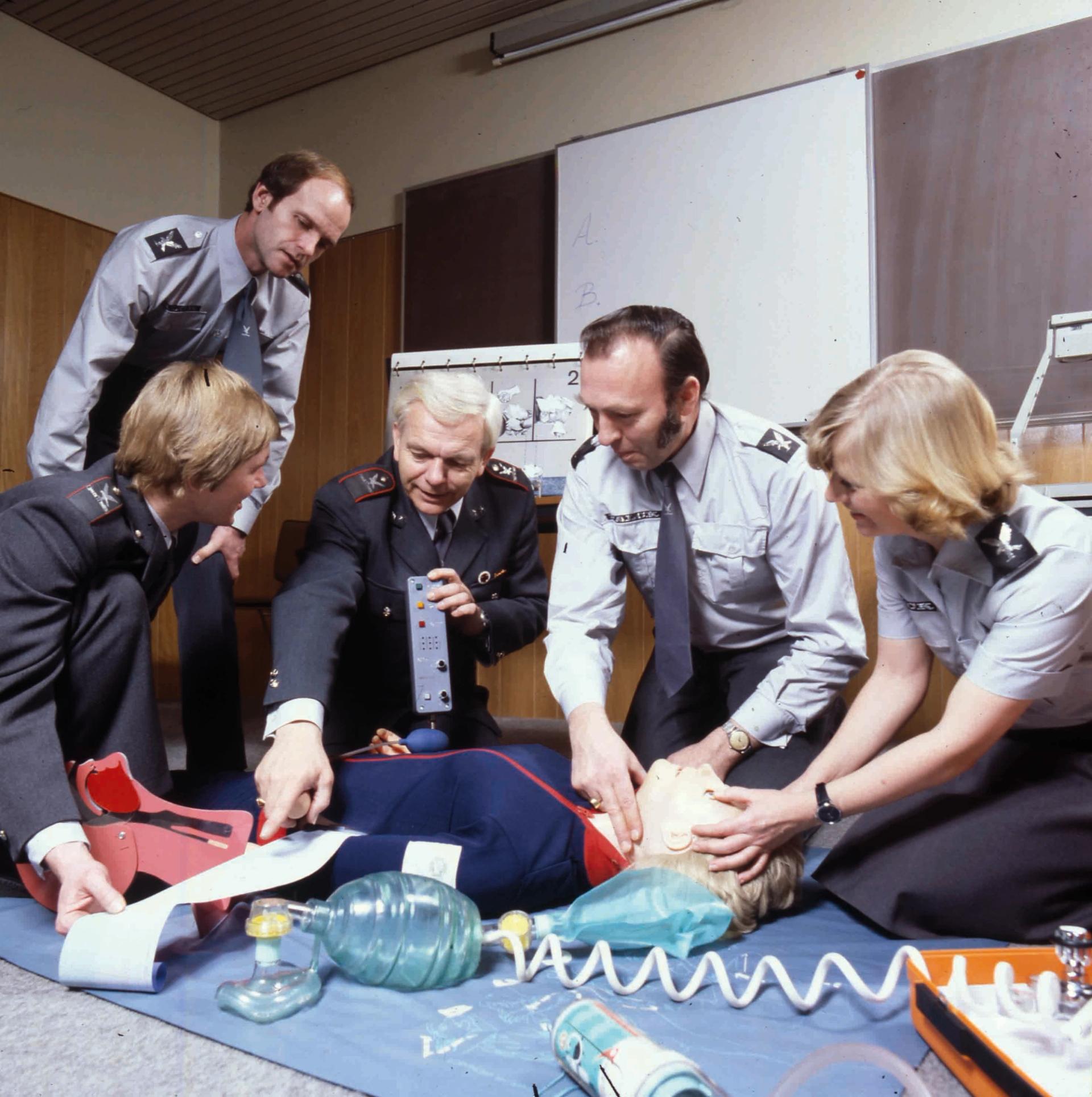 Five people demonstrating a CPR training manikin