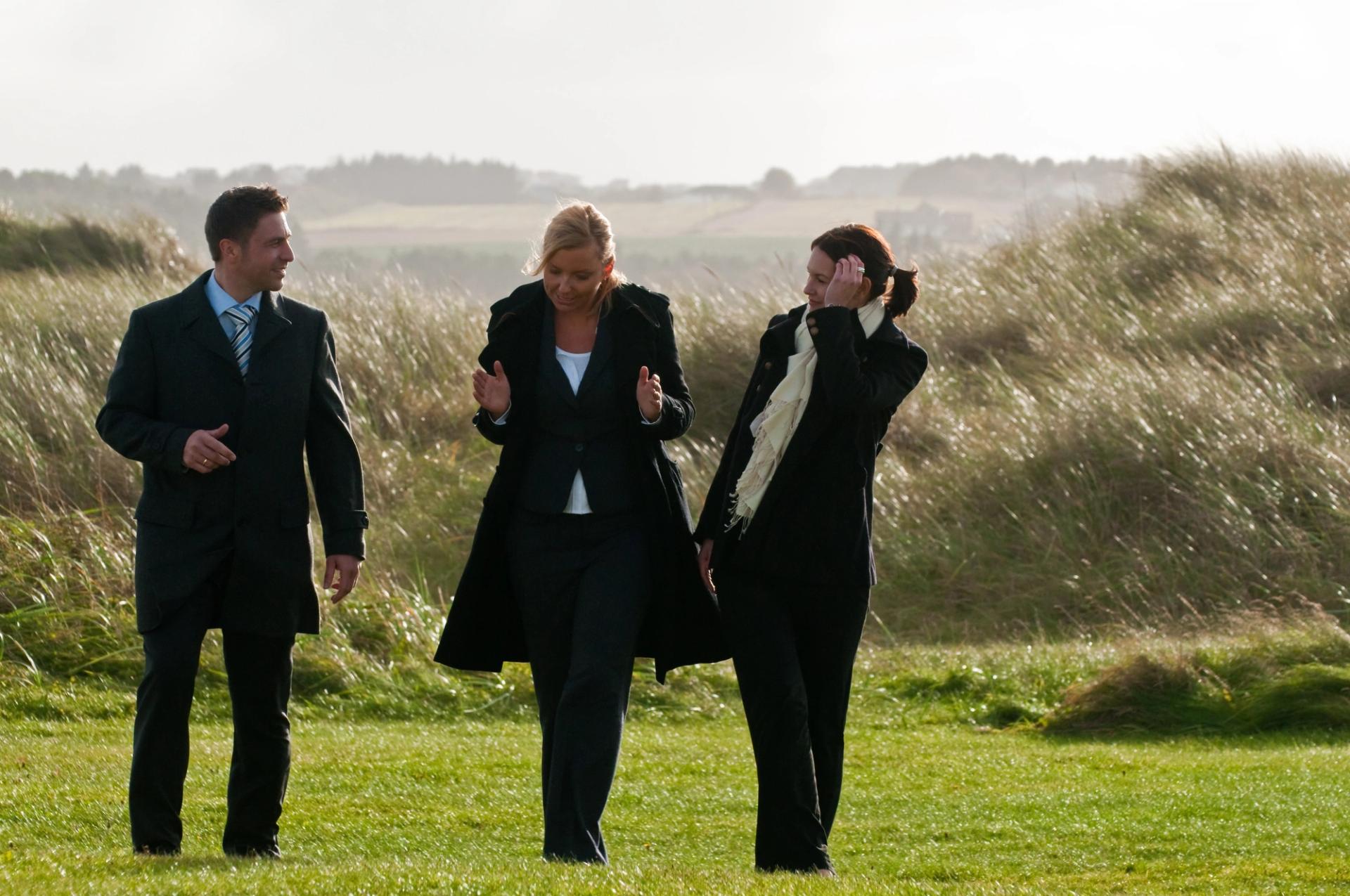 Two women and a man in conversation on a windy green field