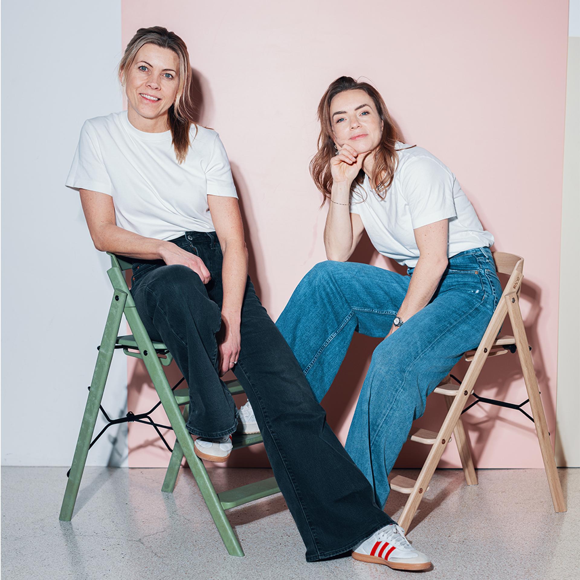 two women in white t-shirts and jeans sitting on high chairs