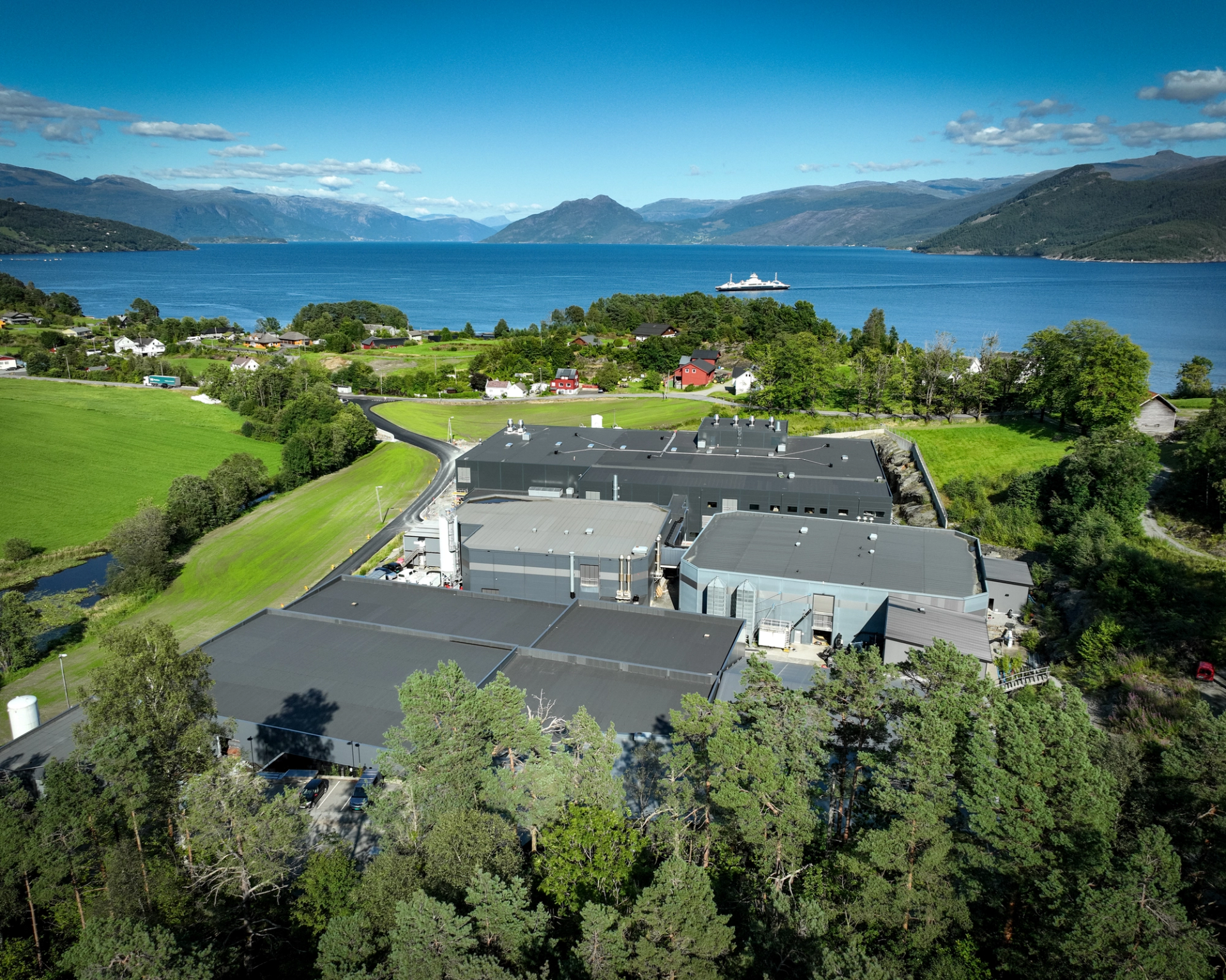 A factory located among green fields looking out over a blue fjord