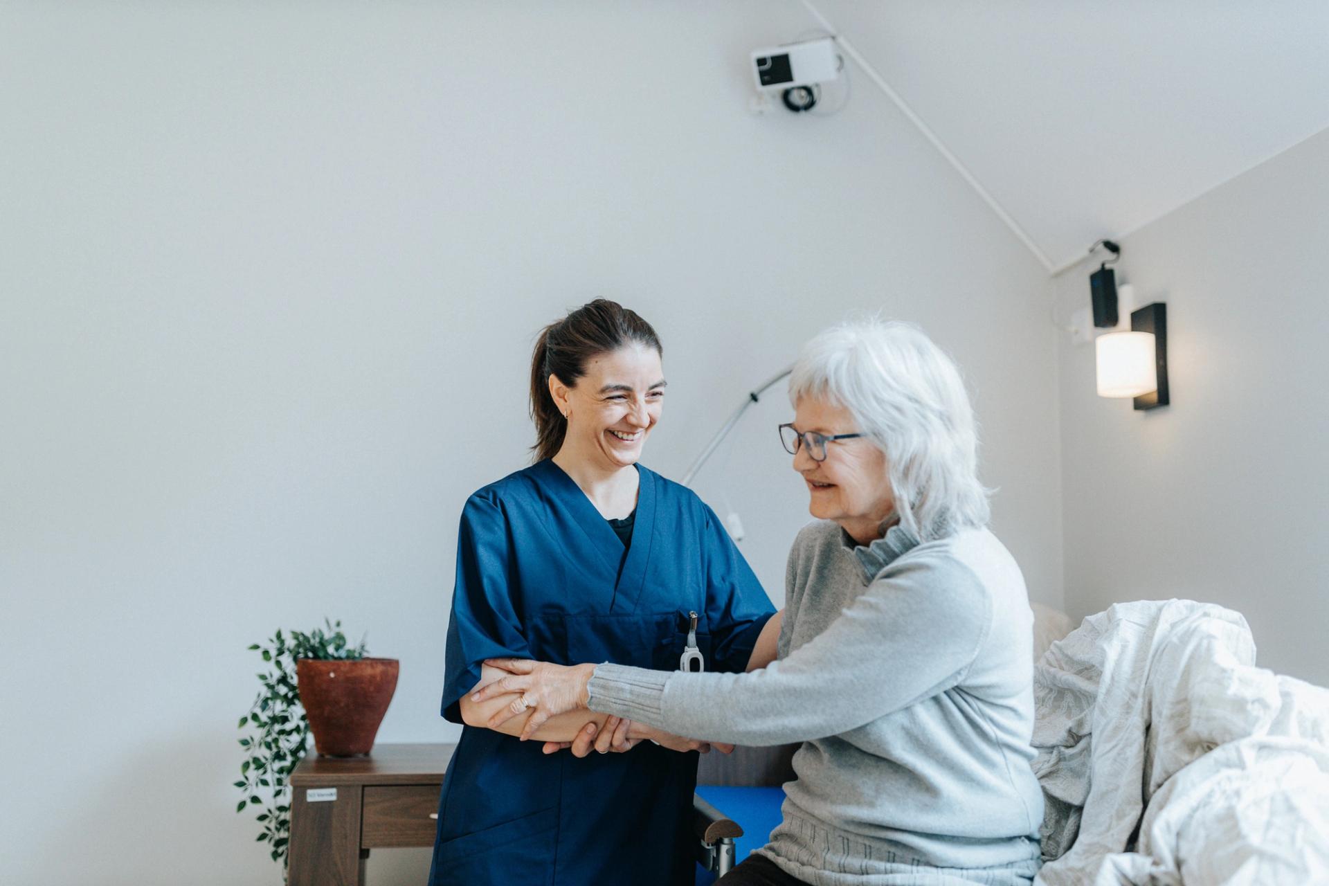 Health care worker helping elder, Made in Norway labelled Sensio RoomMate in background