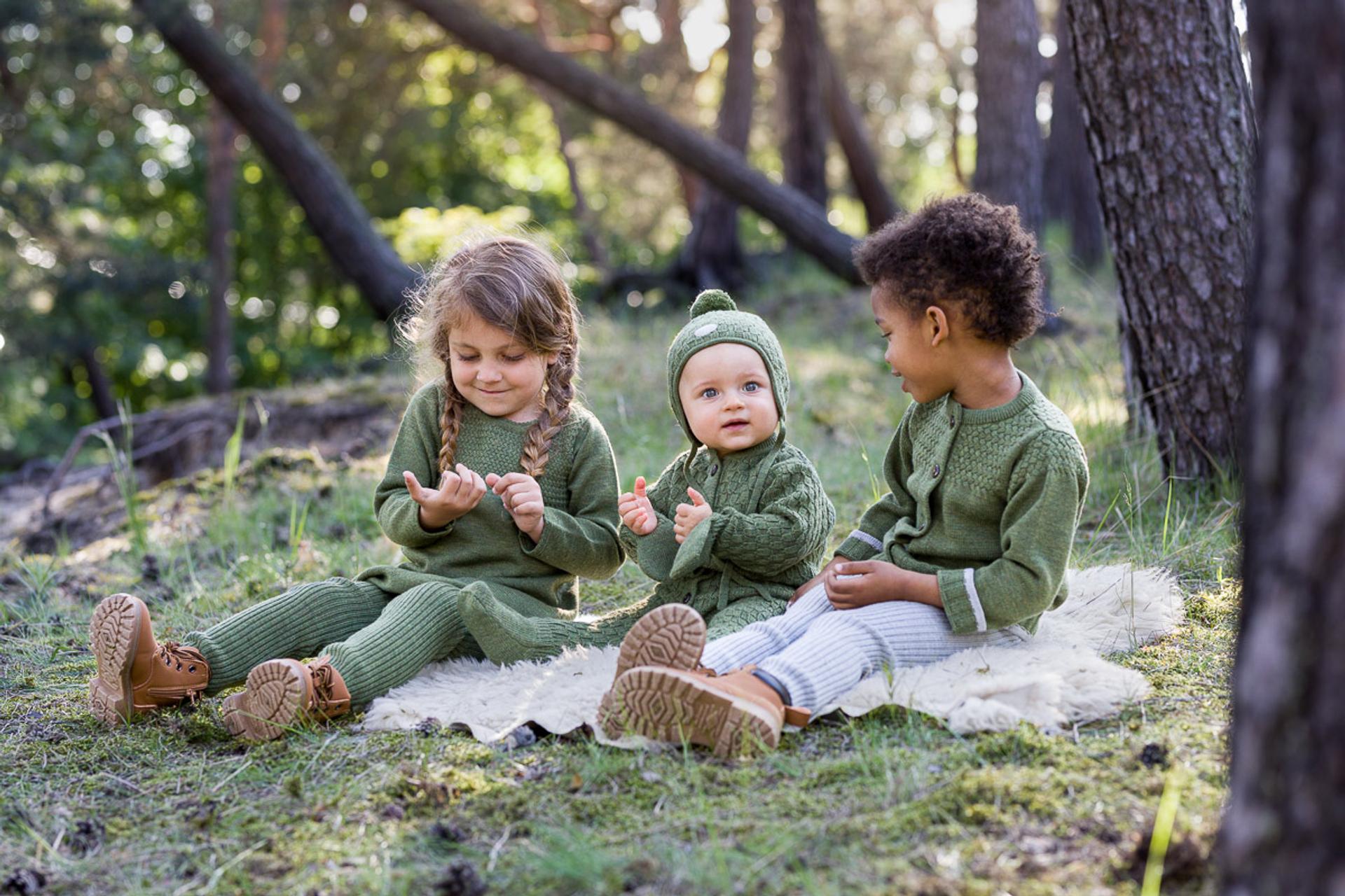 Three young children in green sweaters on the green grass.