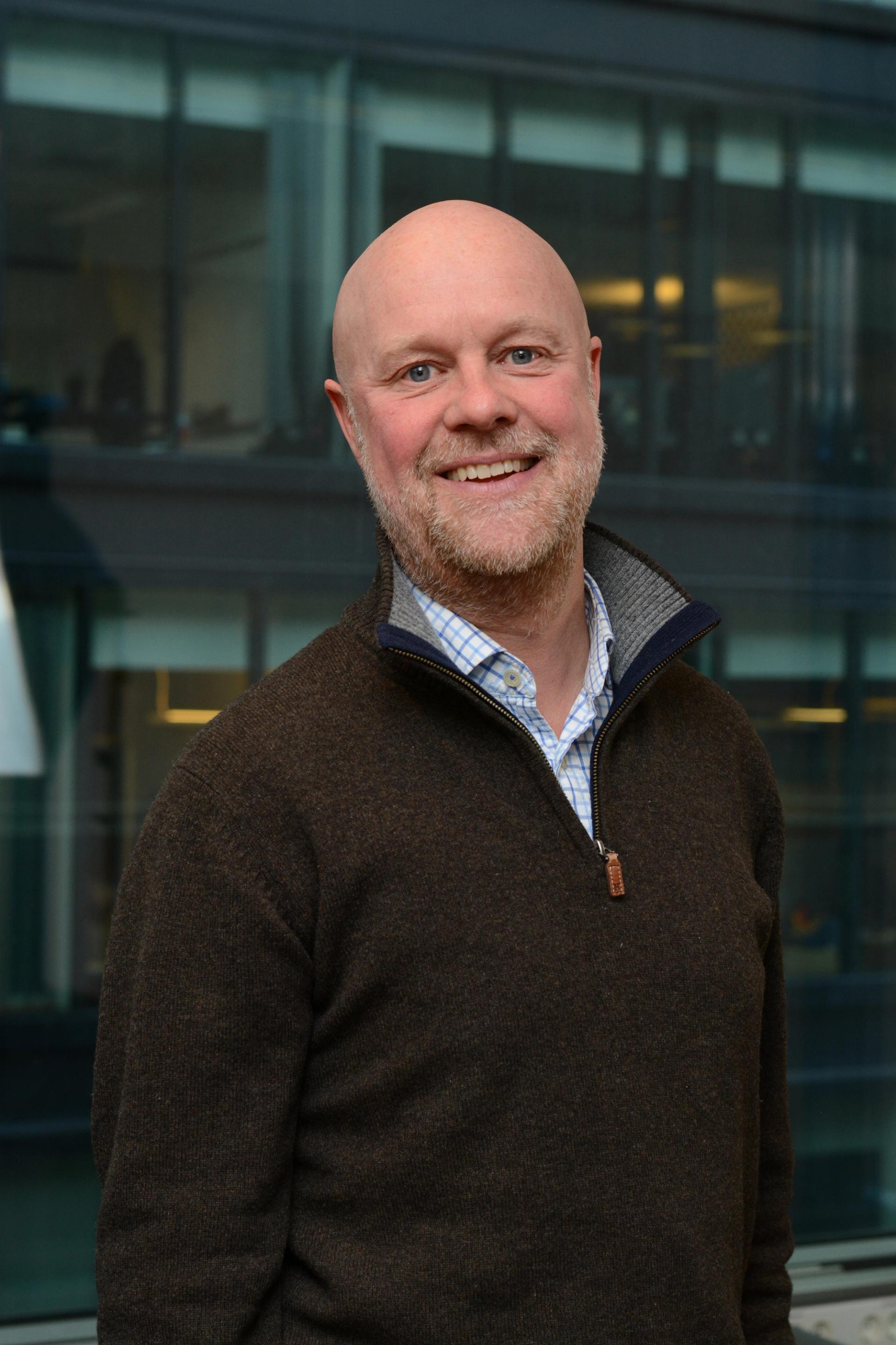 A man smiling straight into the camera, wearing business causal clothing.