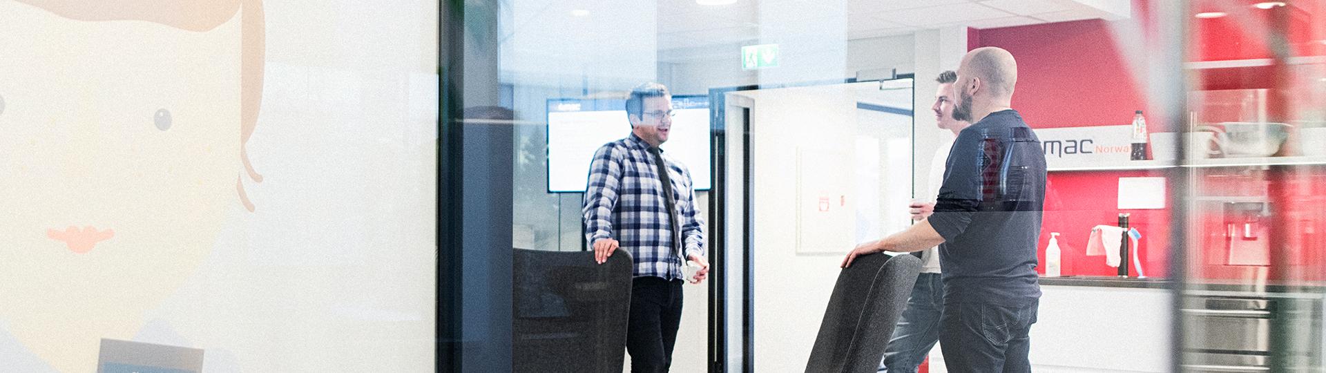 Three men photographed through a glass wall in an office