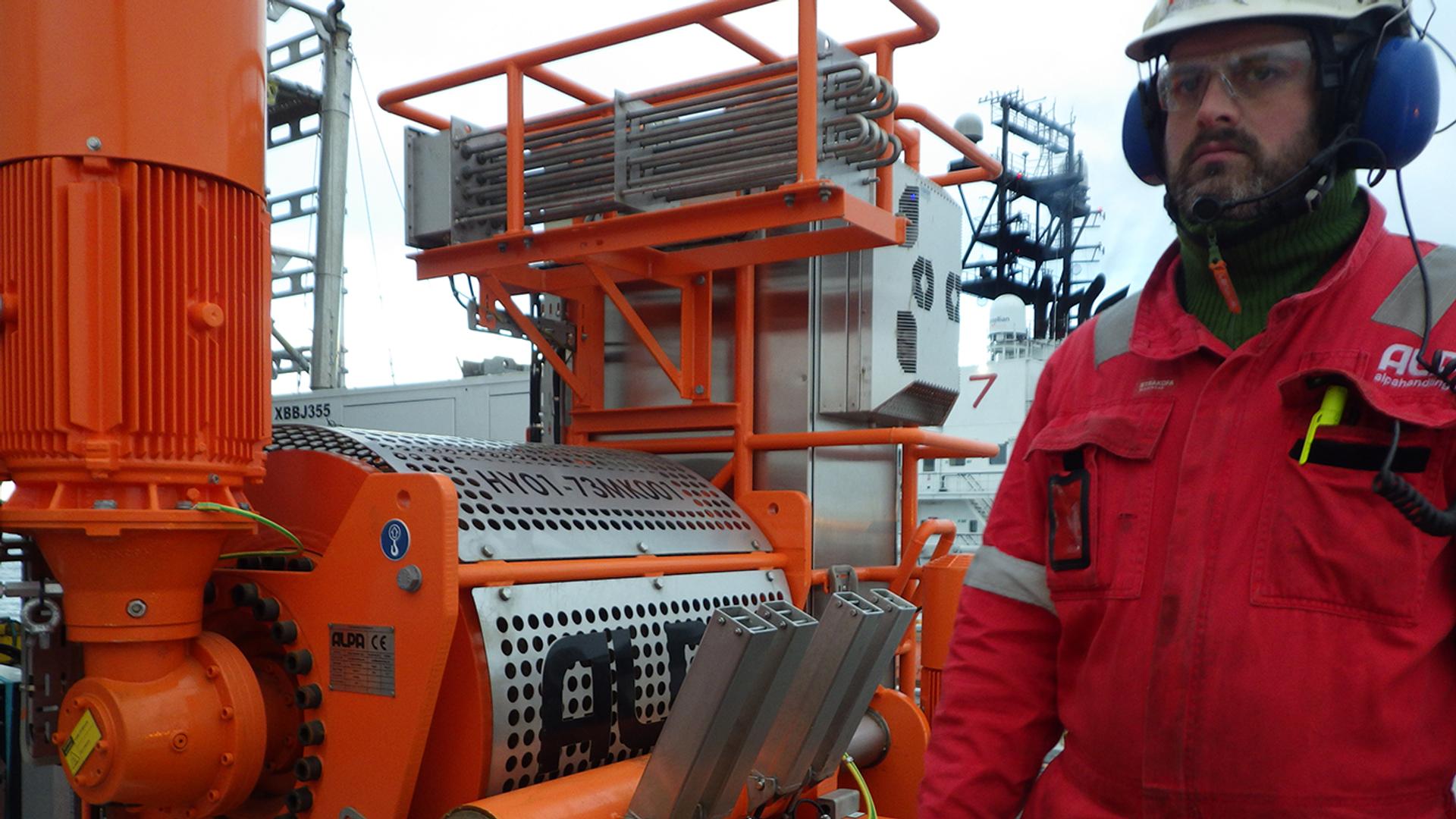Worker in a red suit and white helmet in front of a pull-in unit for offshore wind farms