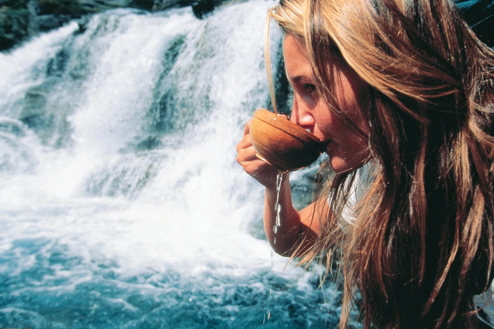 Woman drinking water from a wooden cup at a waterfall