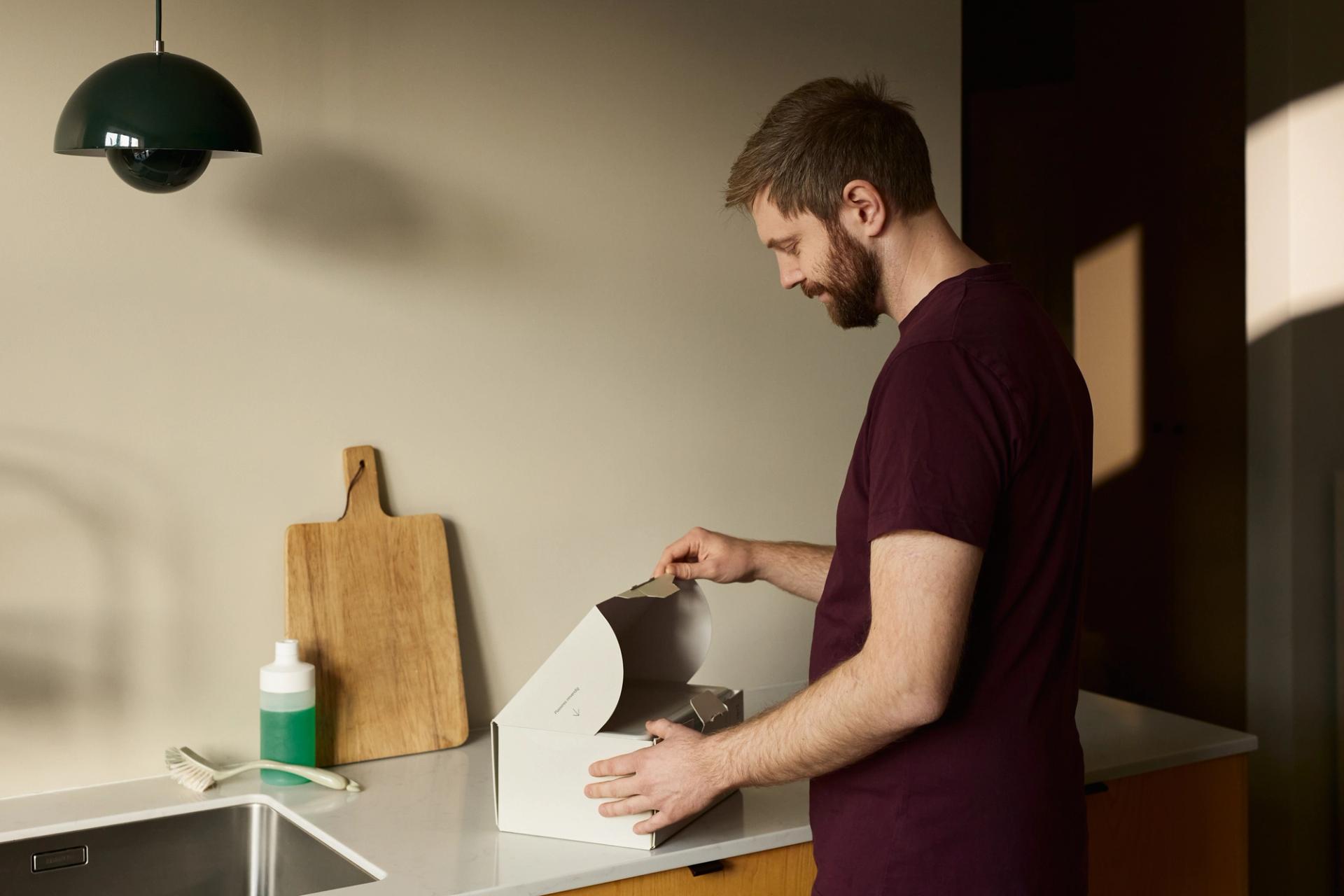 Bearded man opening a cardboard box on a white kitchen countertop
