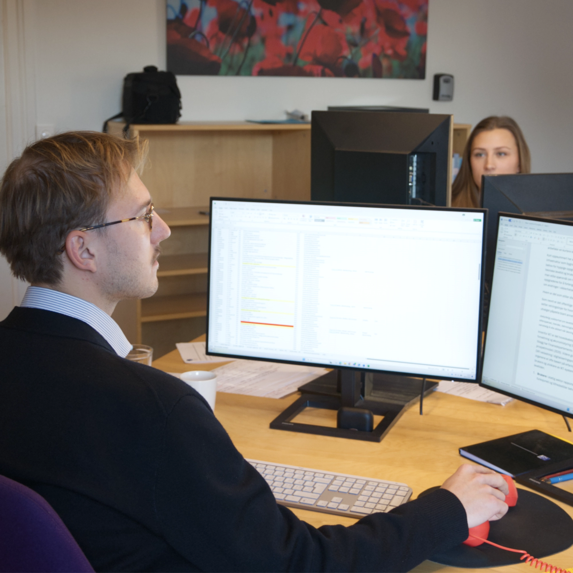 Man with a mustache and glasses in front of two computer screens