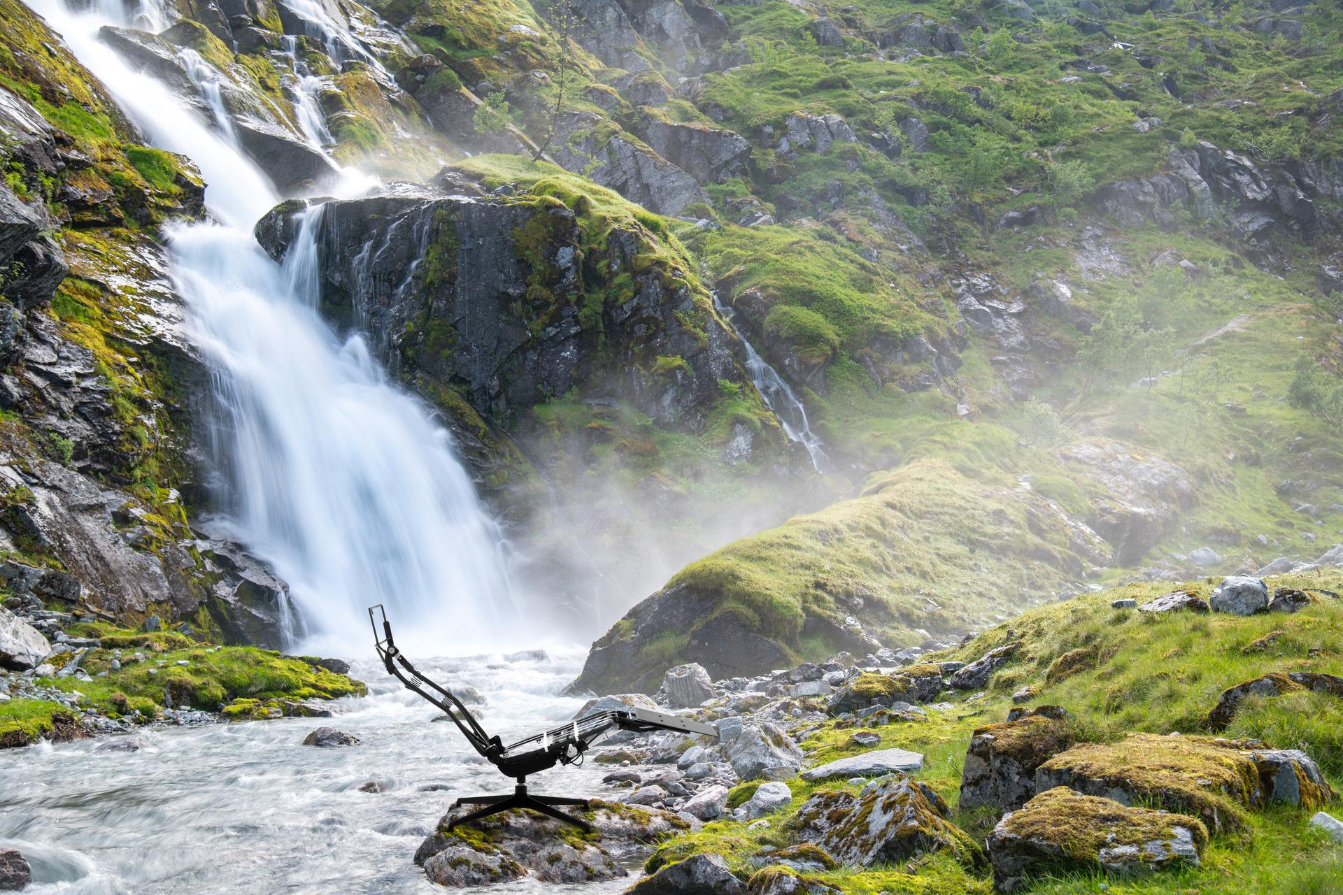 A chair placed out in nature, in front of a waterfall.