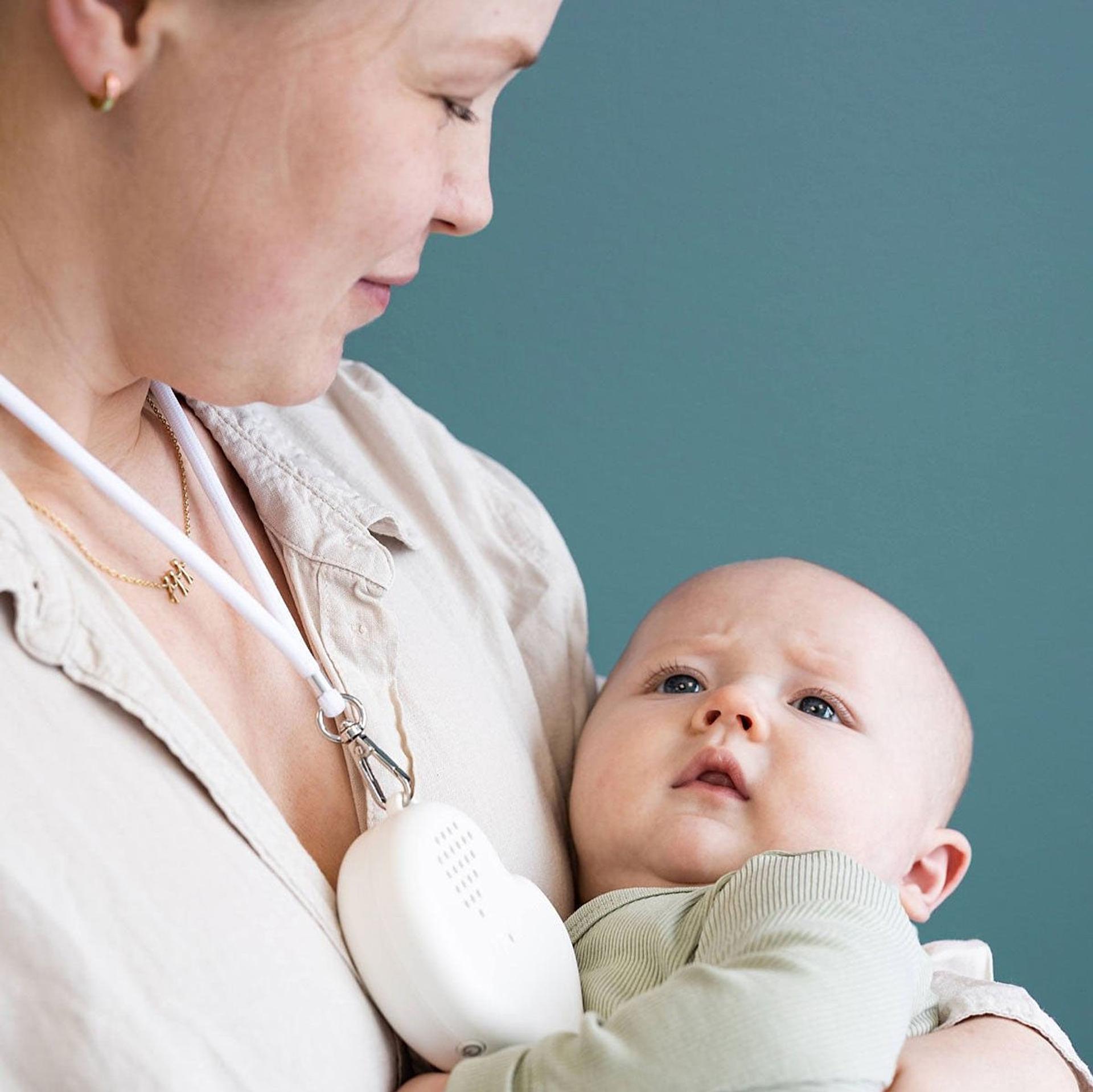 A woman carrying a baby, while having a colic button around her neck soothing the baby.