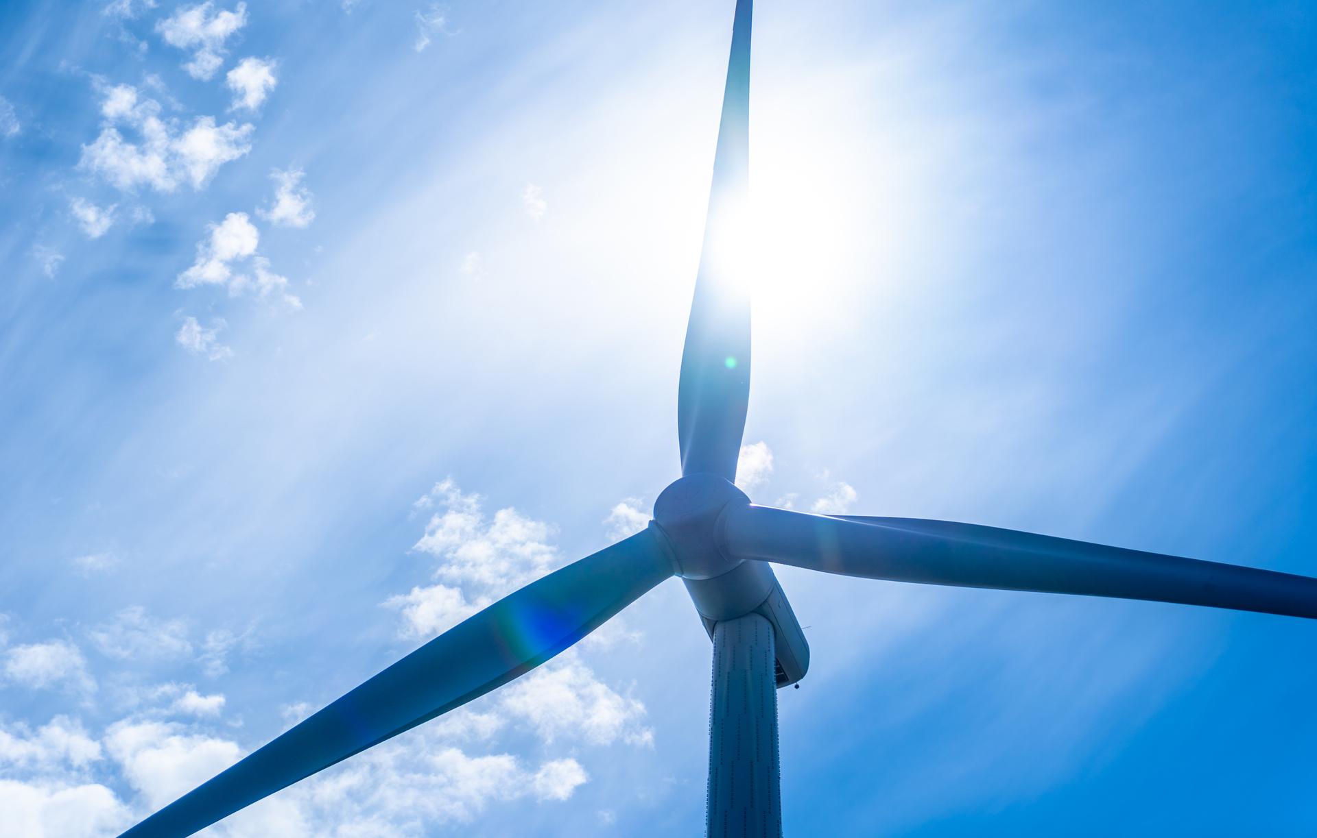 looking up at a wind turbine with the sun behind it