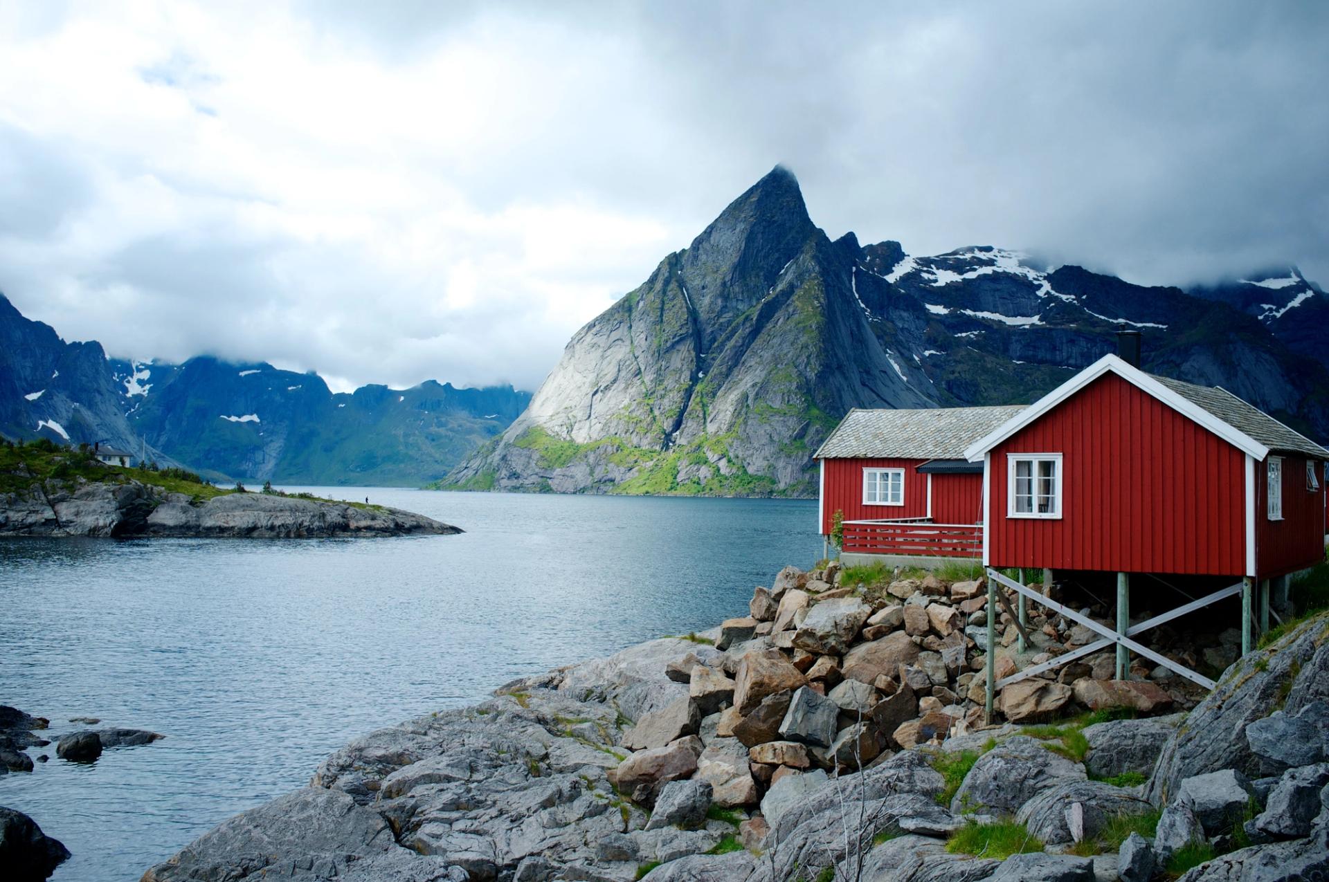 A small red cabin along side a fjord with mountains in the background