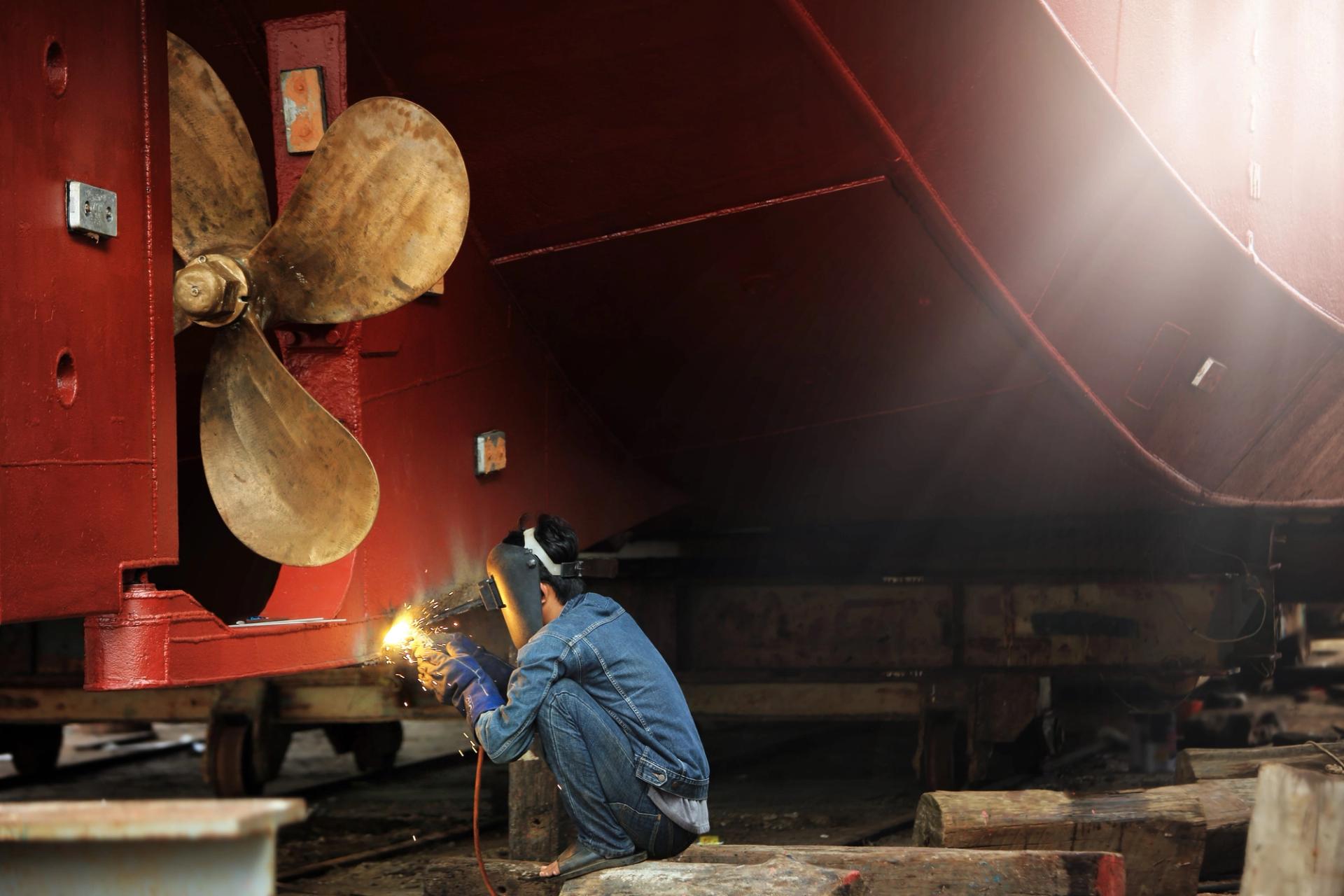 Man welding a bronze propellor on a red ship