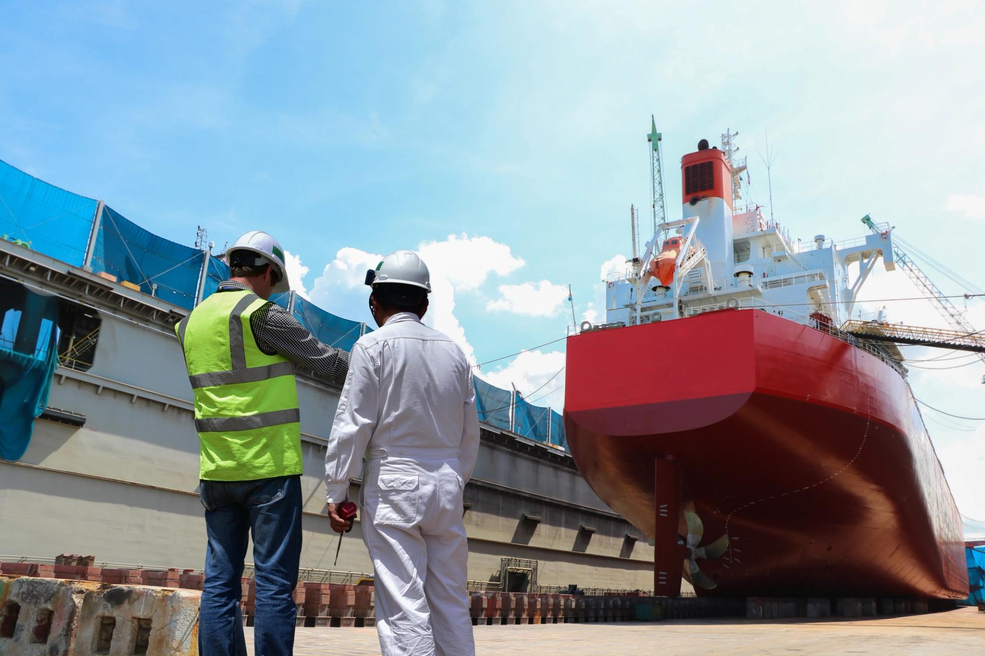 Two men in hard hats in front of a red ship