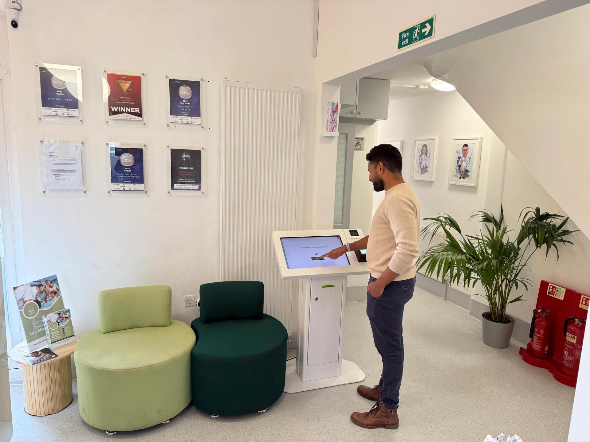 Man with dark hair and beard in a white sweater checking in at a doctor's office with a self-service kiosk