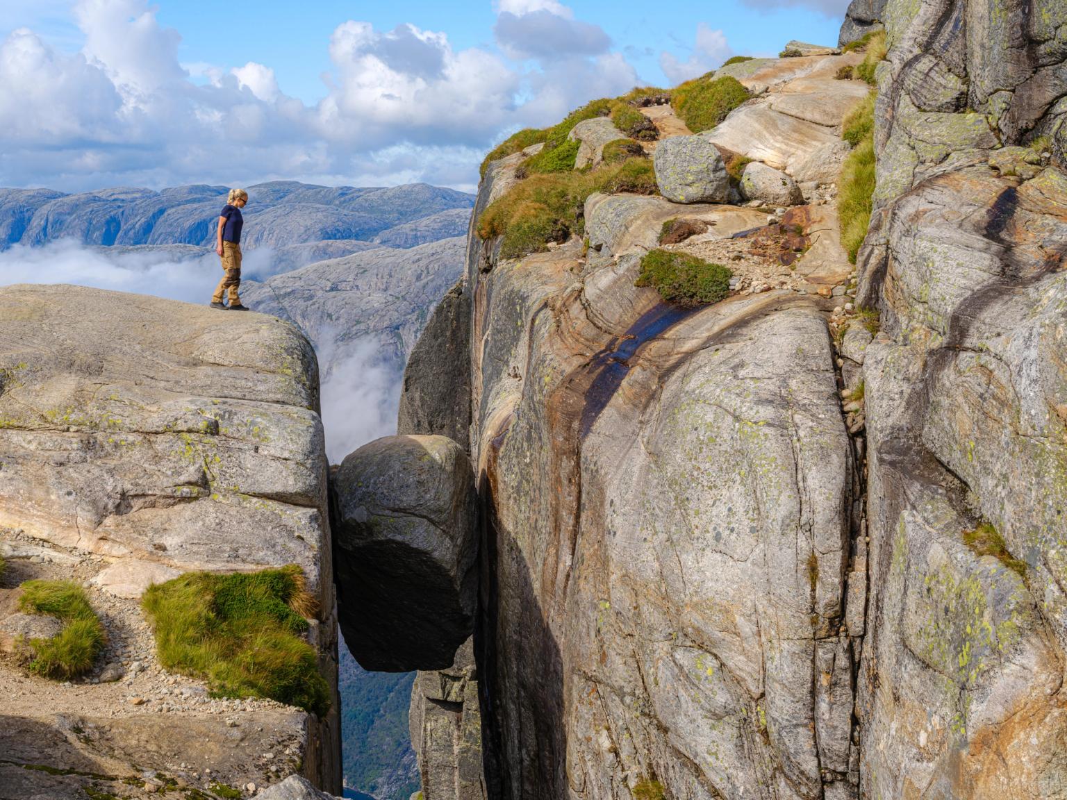 Woman standing on a cliff overlooking the Kjerag boulder
