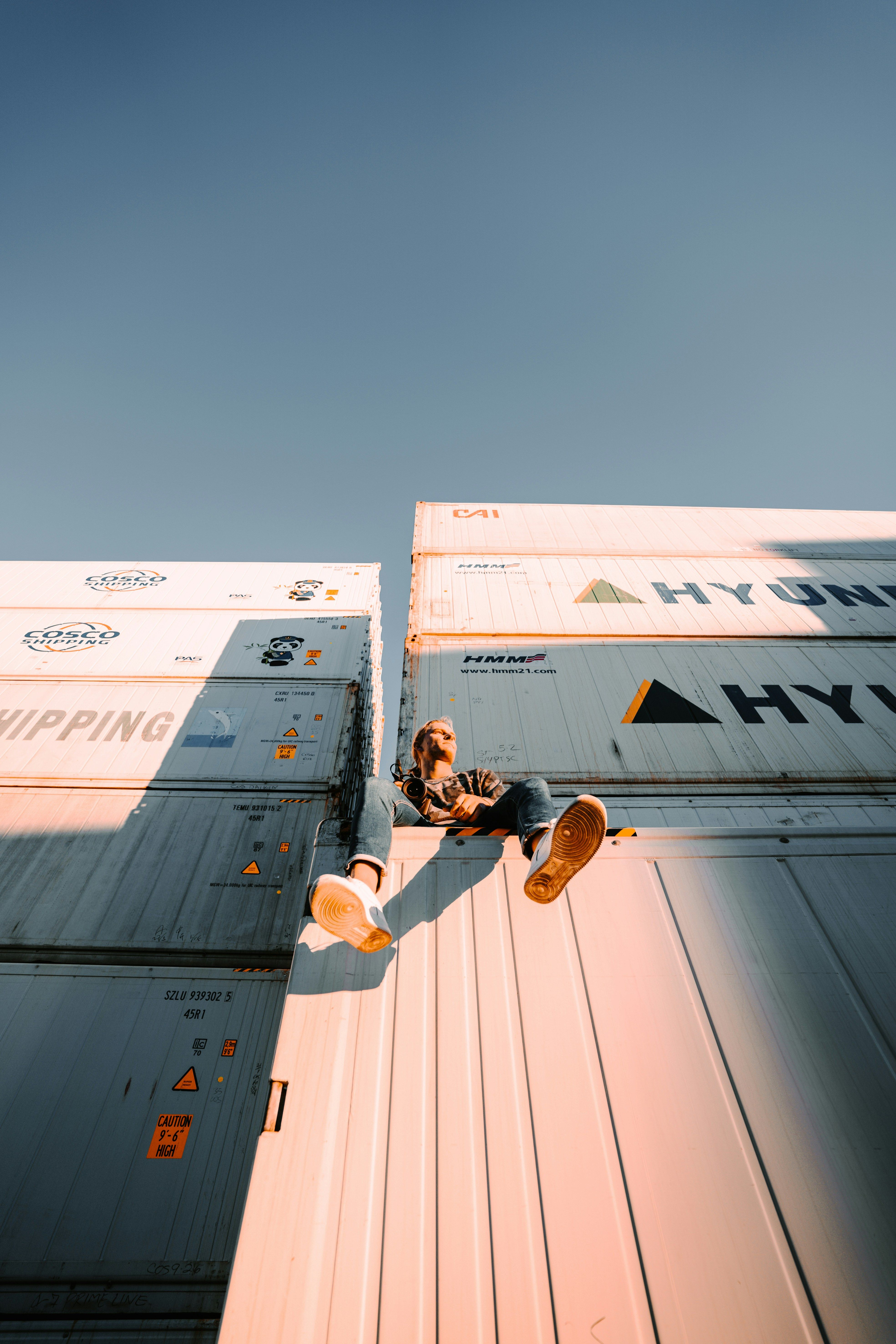 Mann som sitter på en haug containere på en havn i solnedgangen