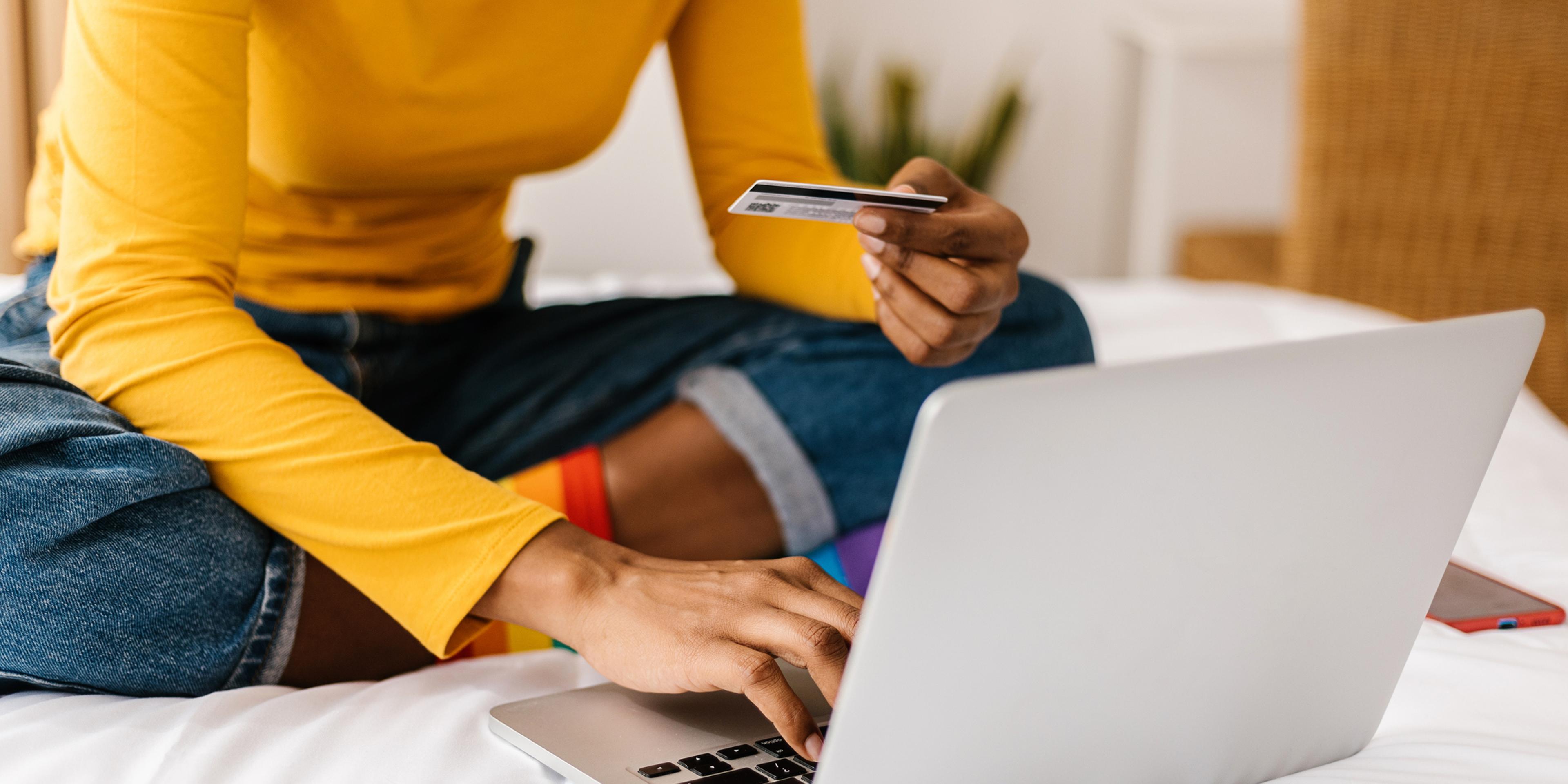 Nærbilde av dames hånd som holder et kredittkort for å utføre kjøp på laptop. E-handel og shopping online som konsept.