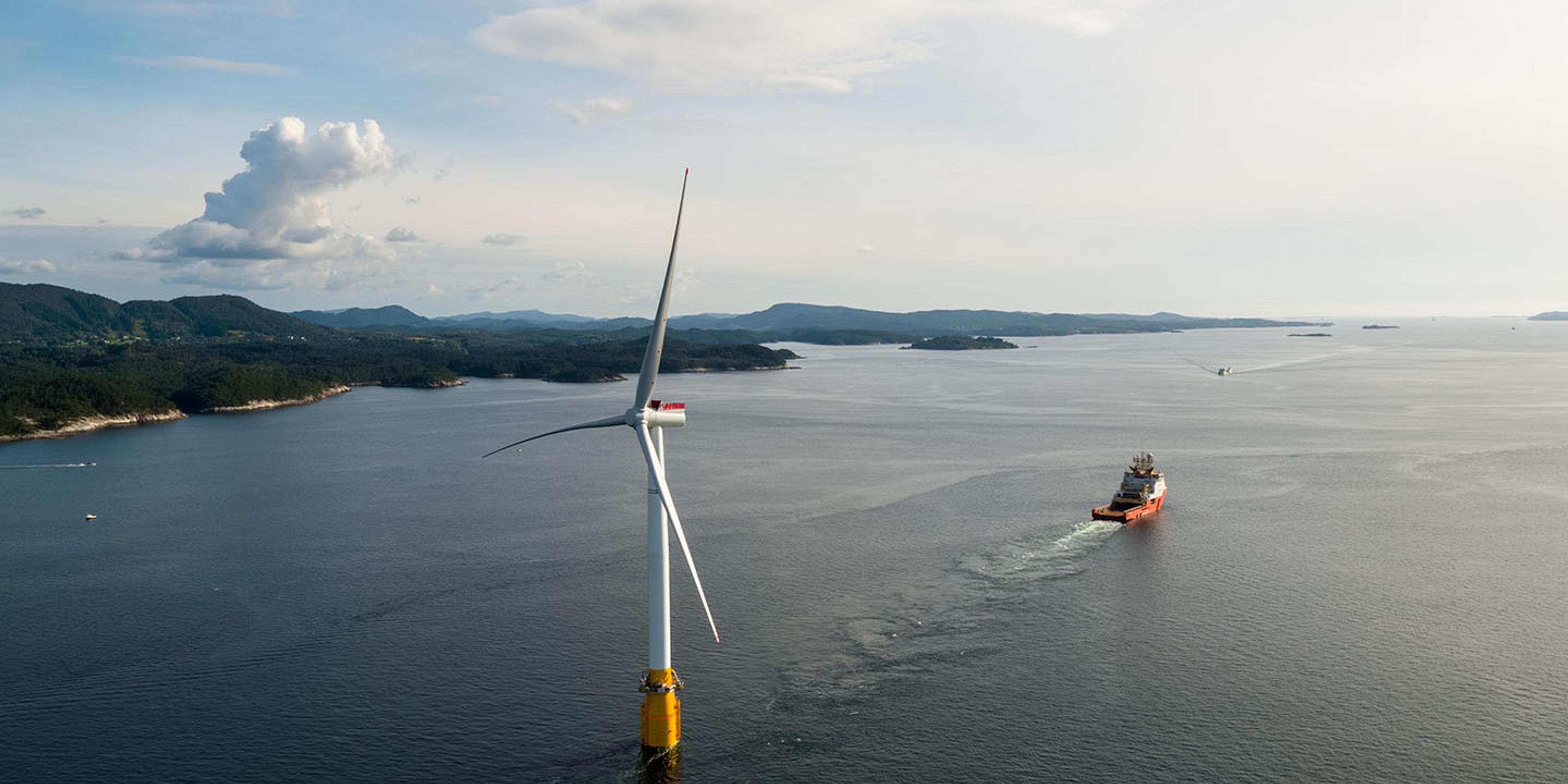 Floating offshore wind turbine in coastal setting with offshore vessel in the distance