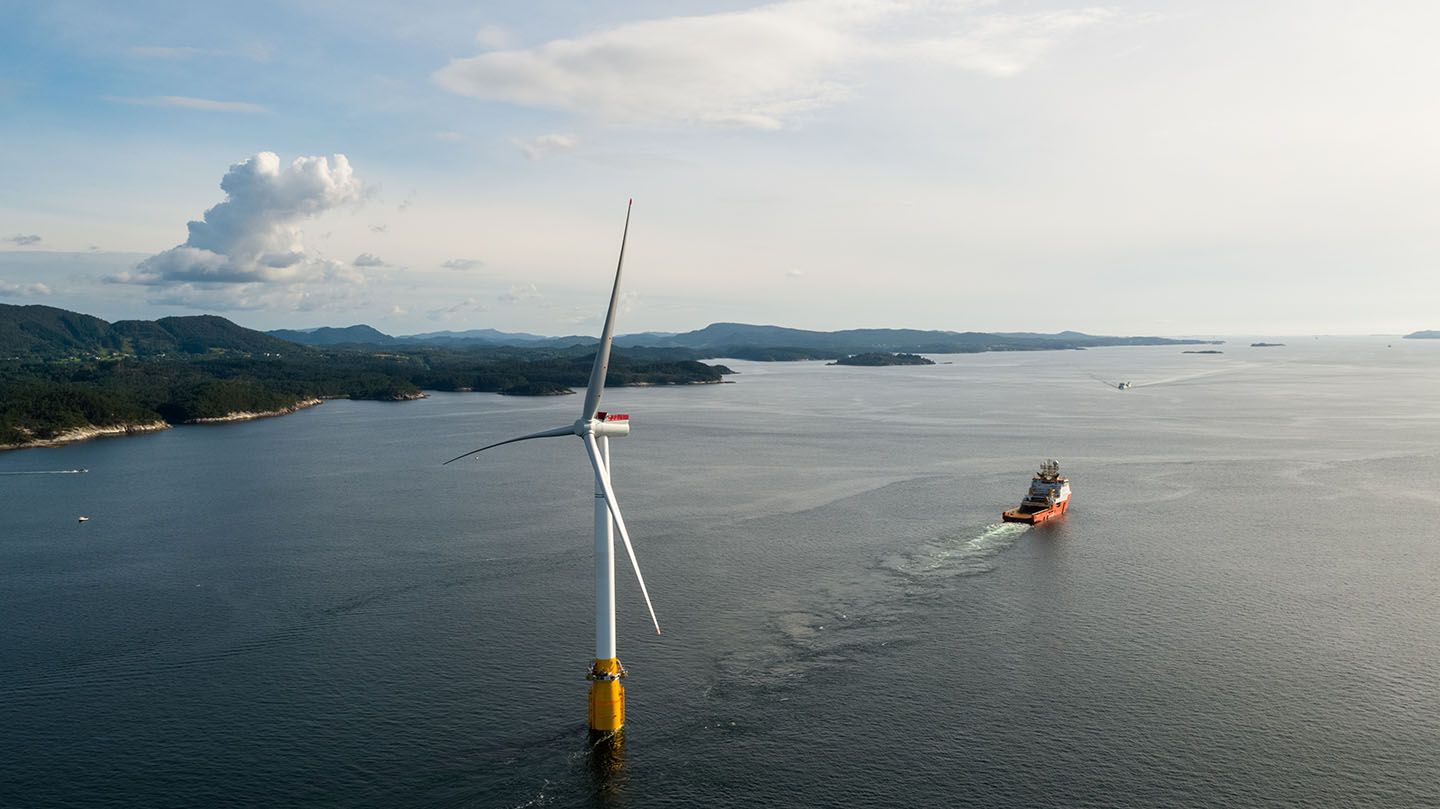 Floating offshore wind turbine in coastal setting with offshore vessel in the distance