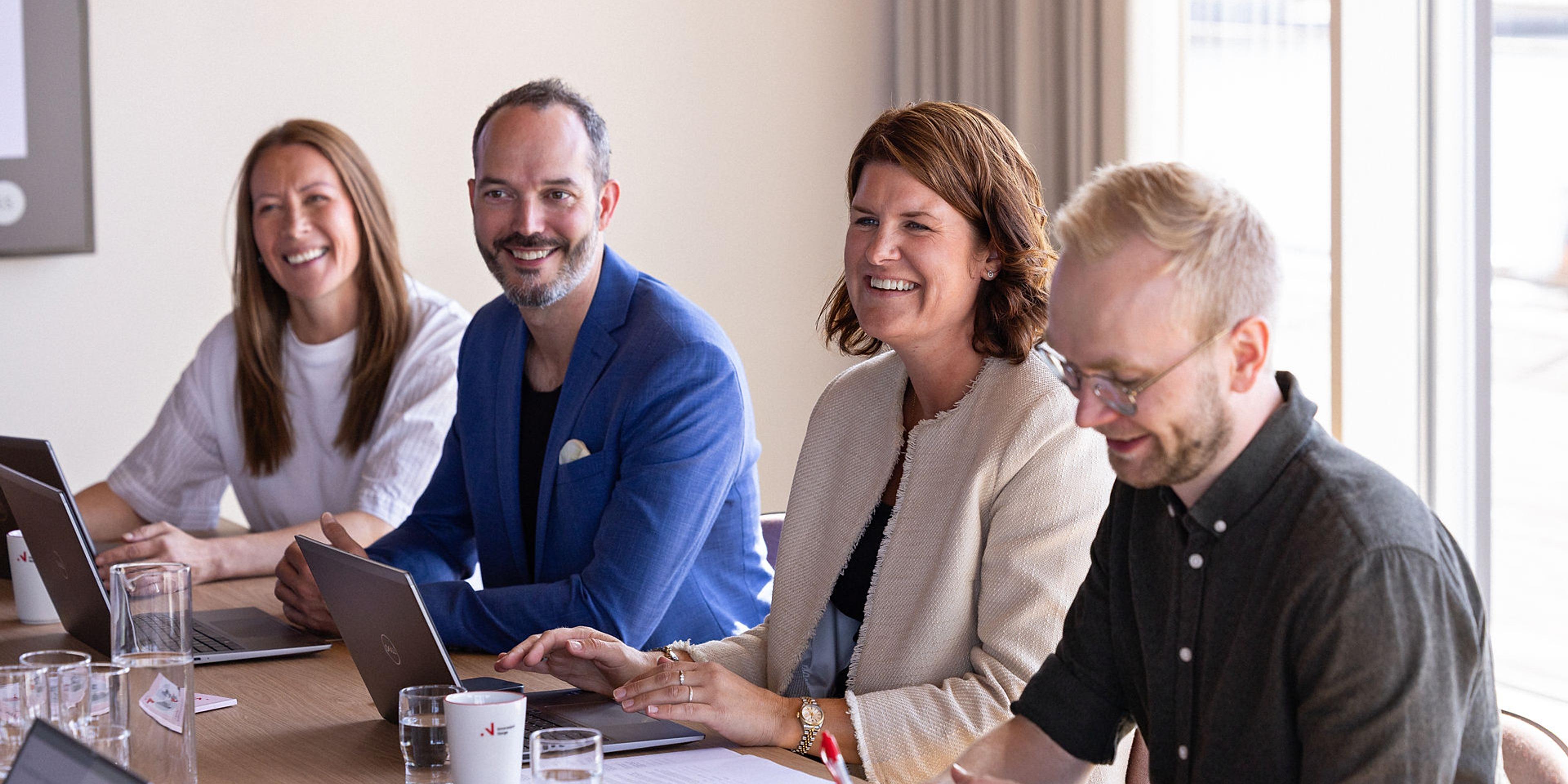 En gruppe mennesker ved et møtebord som smiler