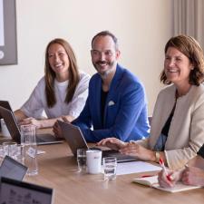 En gruppe mennesker ved et møtebord som smiler