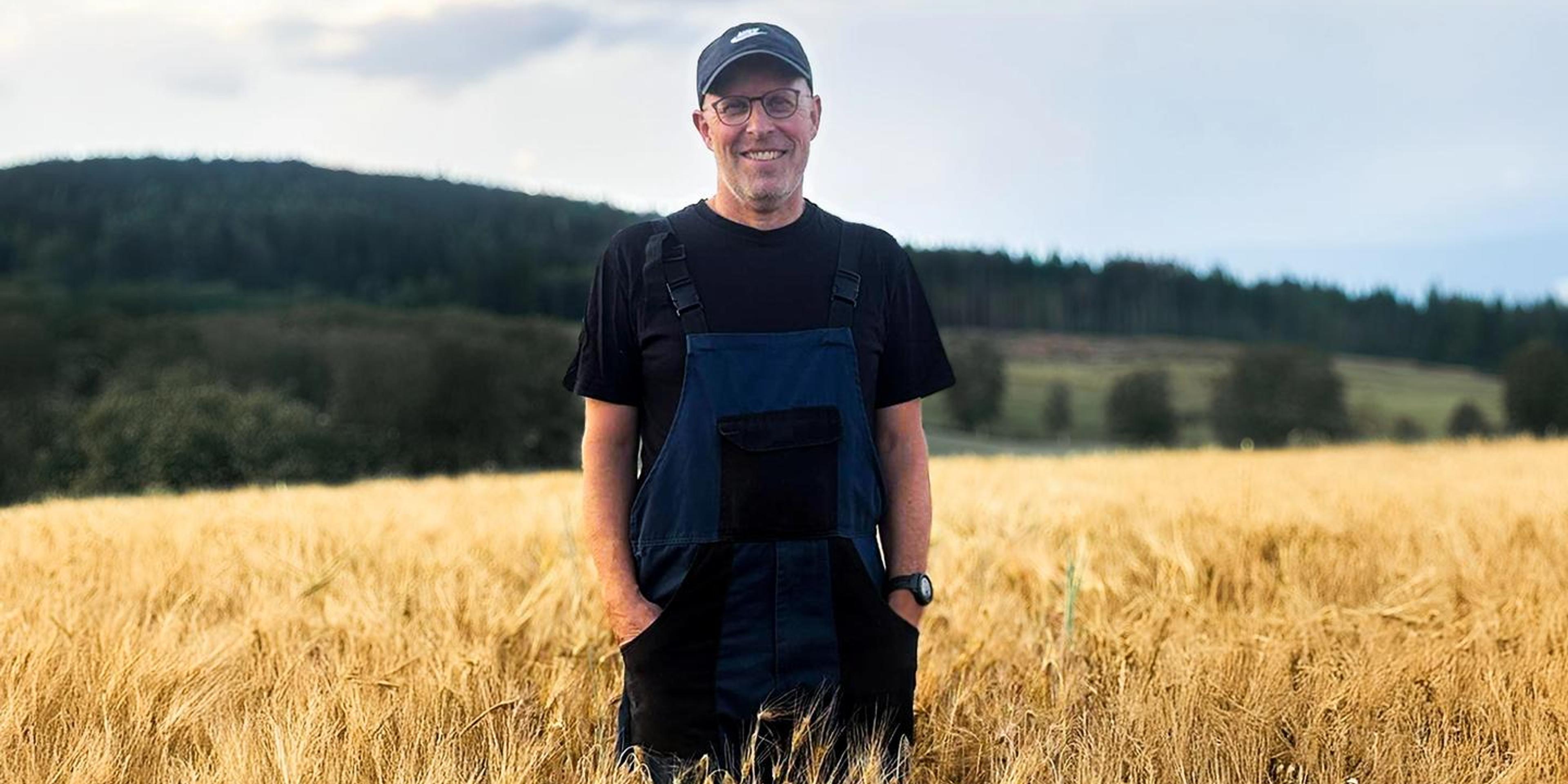 Glad bonde stående i åker.