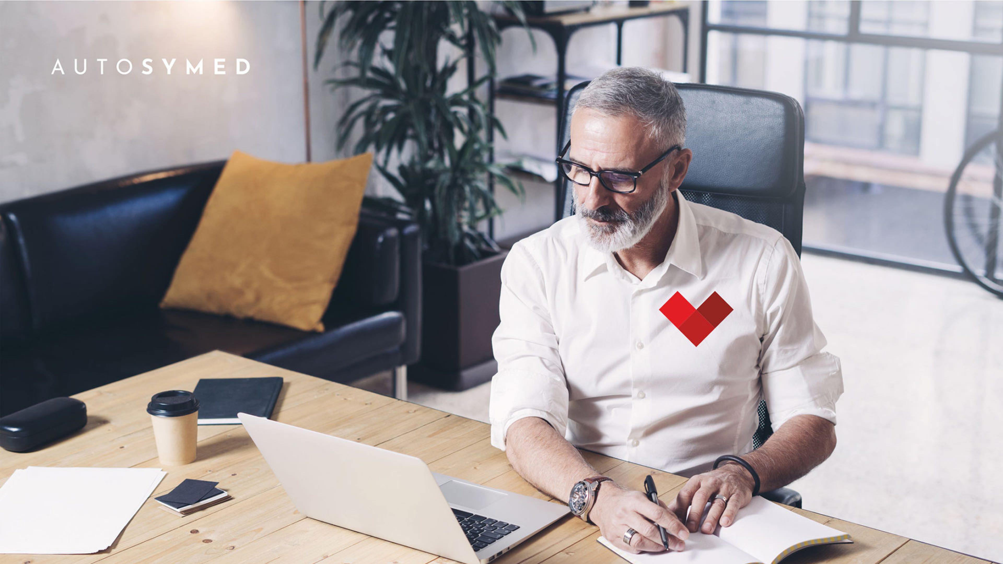 A man sitting in front of a computer writing down notes. The logo for Autosymed is in the picture.