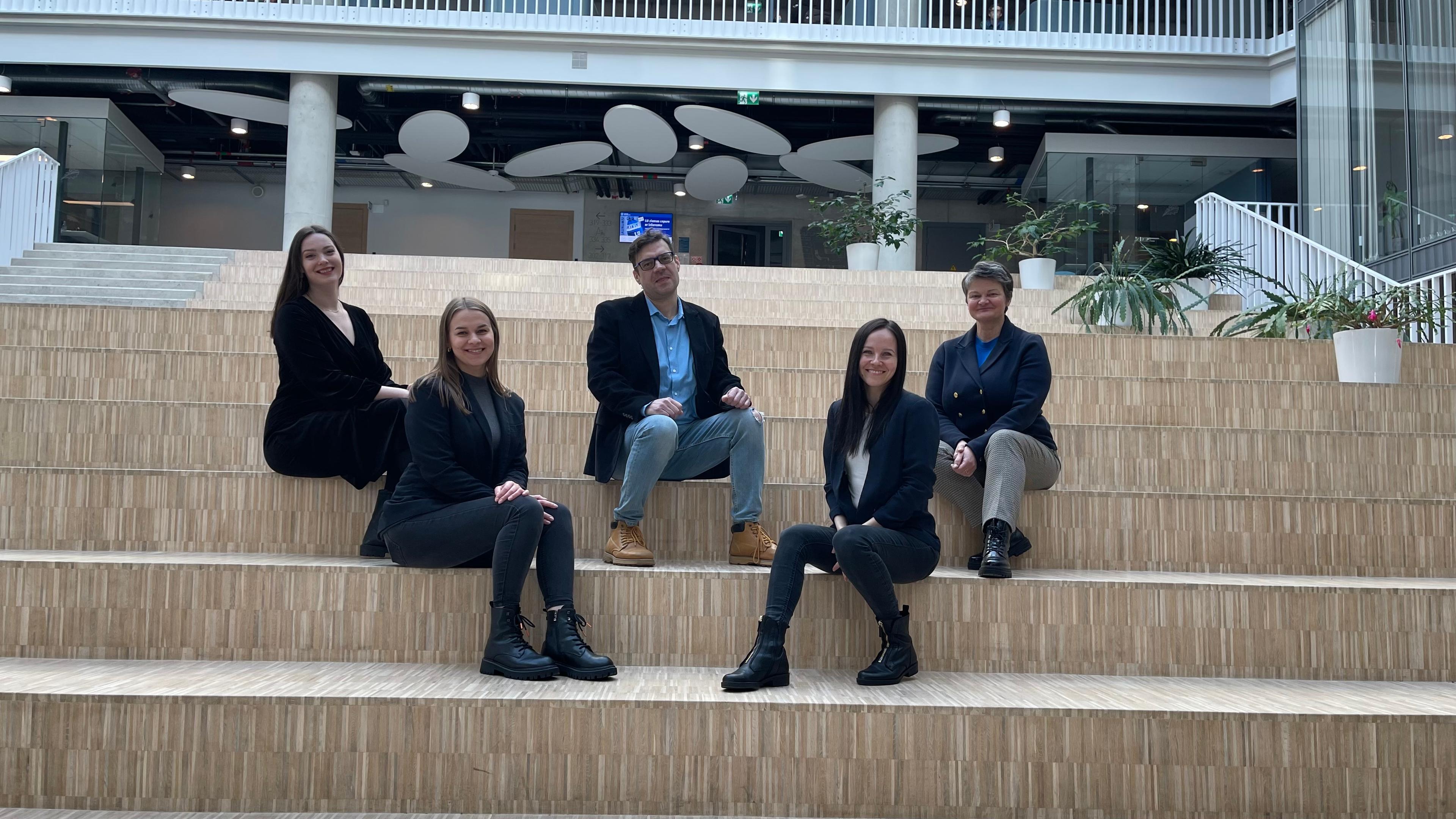 A photo of the five members of technology Business Center. 5 smiling people sitting in the stairs, with the head of TBC in the middle