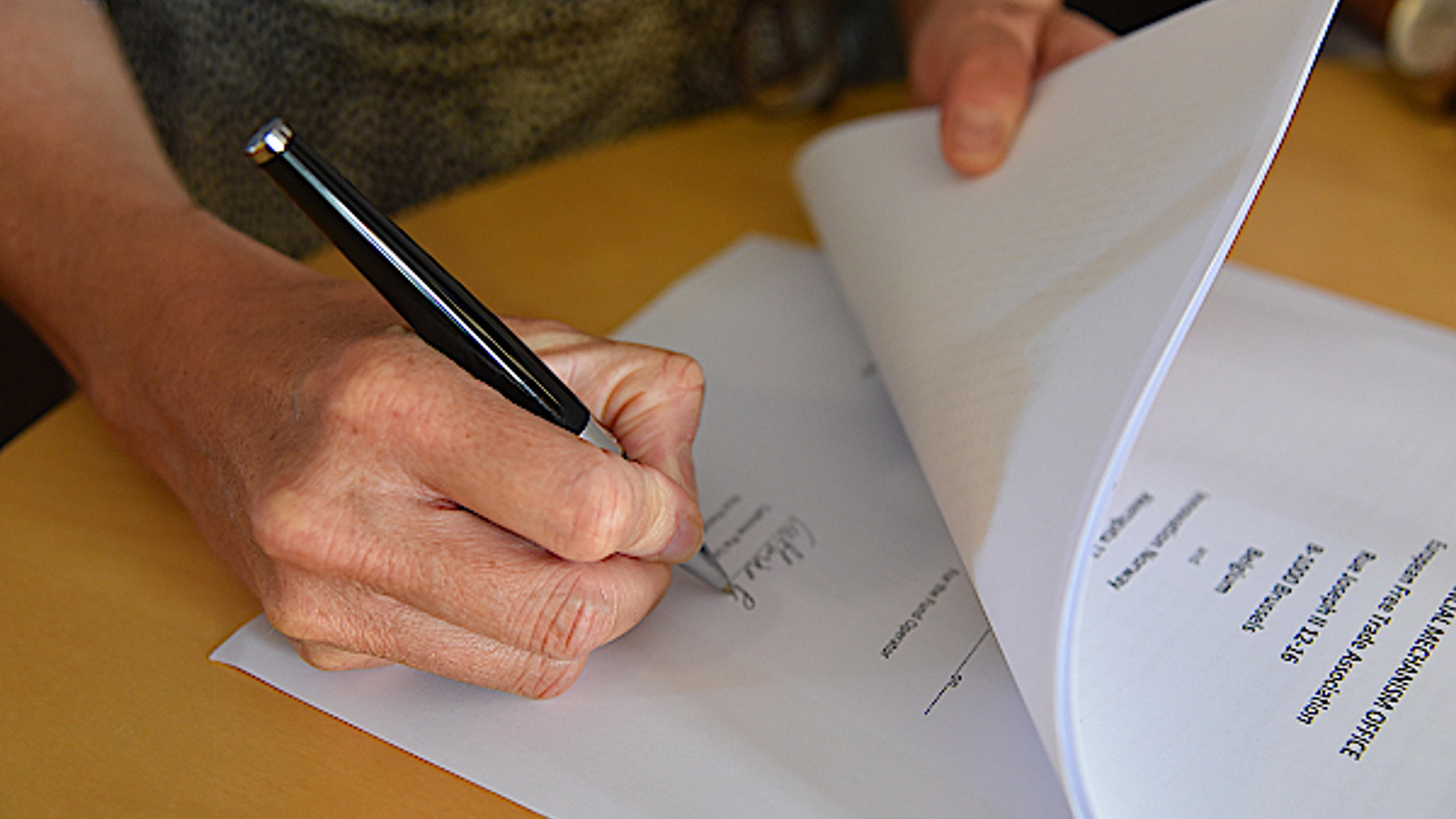 En hånd som holder en penn og signerer papirer