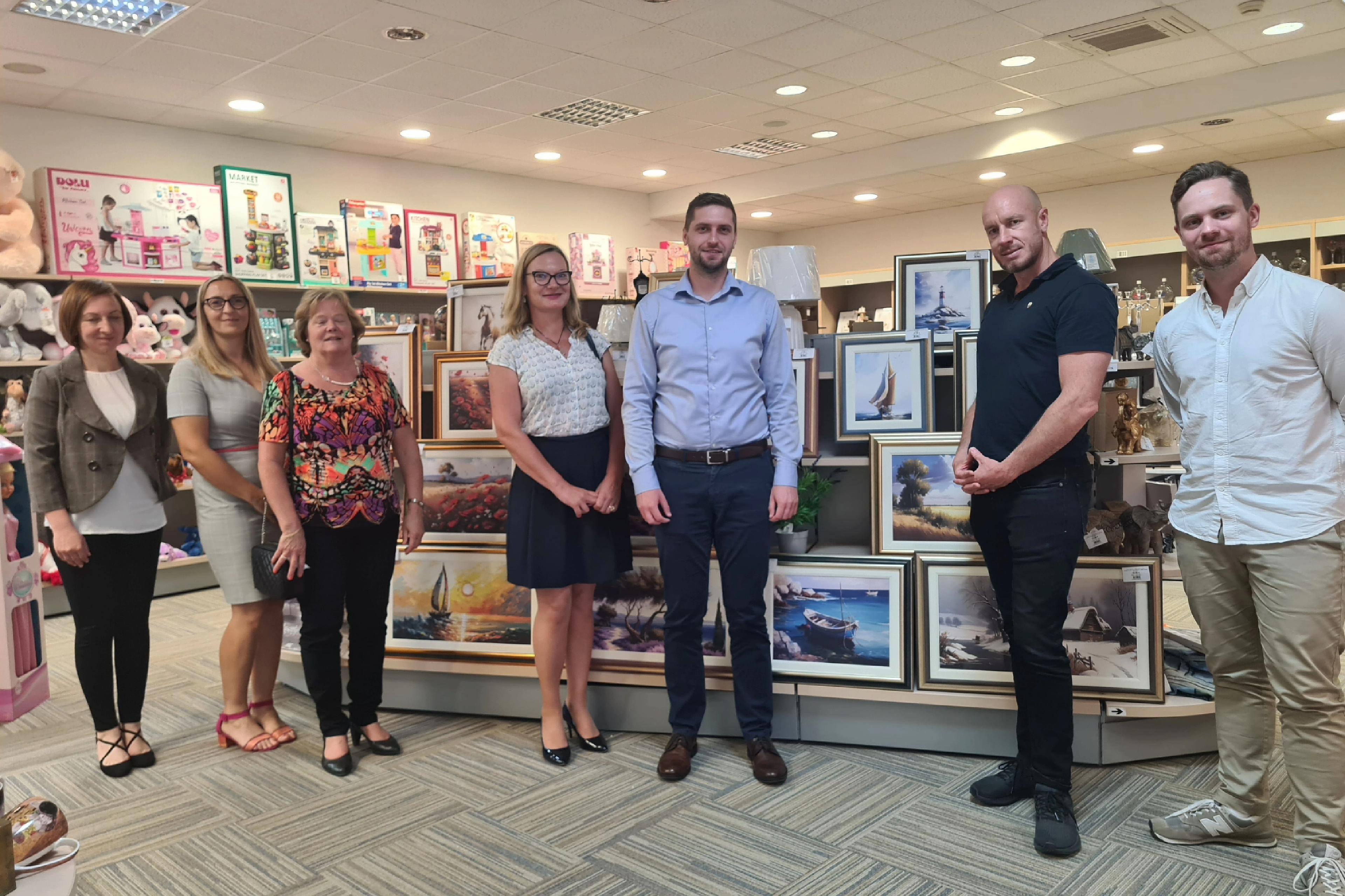 Innovation Norway and the Financial Mechanism Office visiting the project. 7 people smiling in one of the stores of KB smiling in front of paintings sold by KB