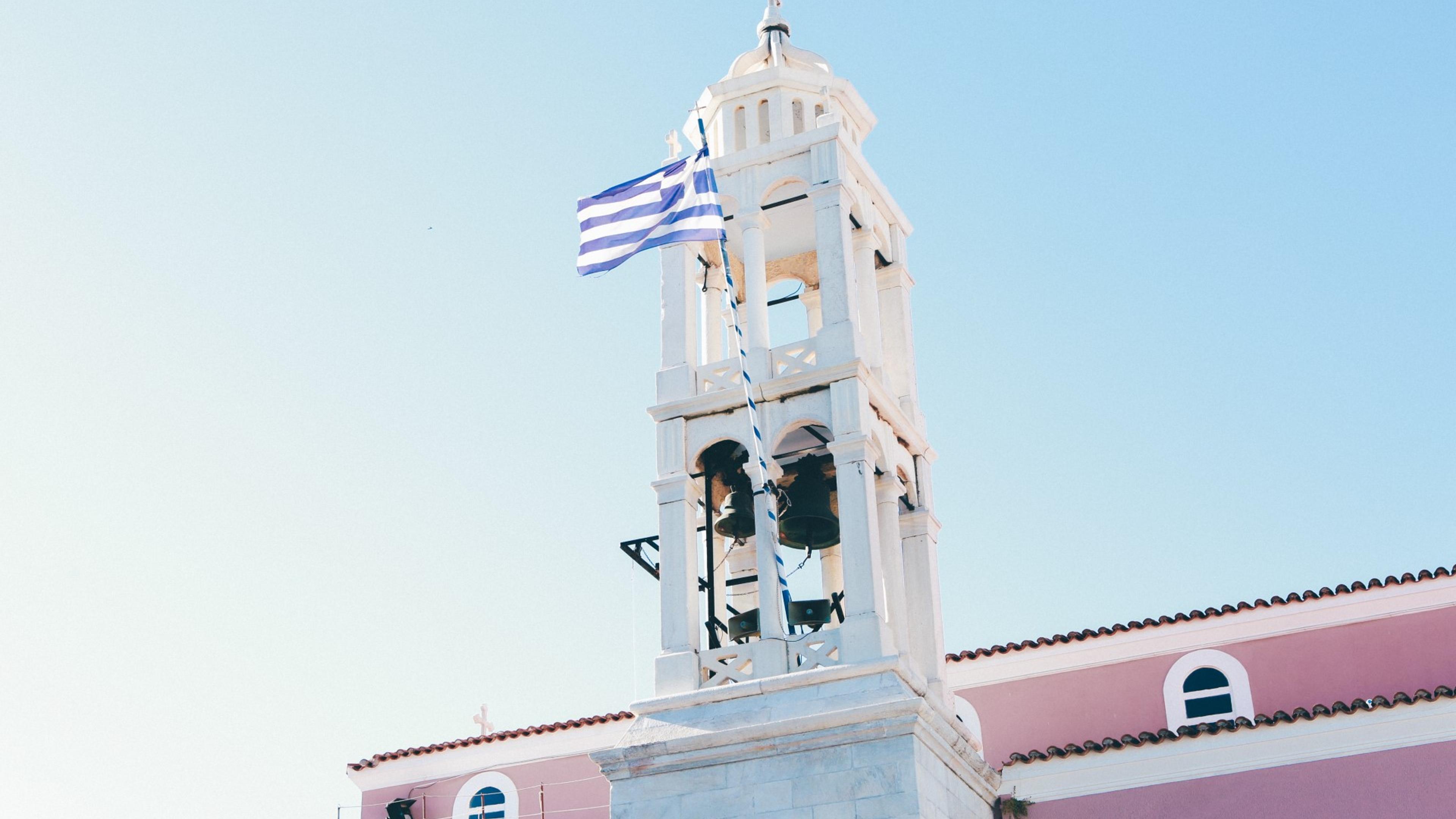Kirketårn mot blå himmel, dekorert med det greske flagget