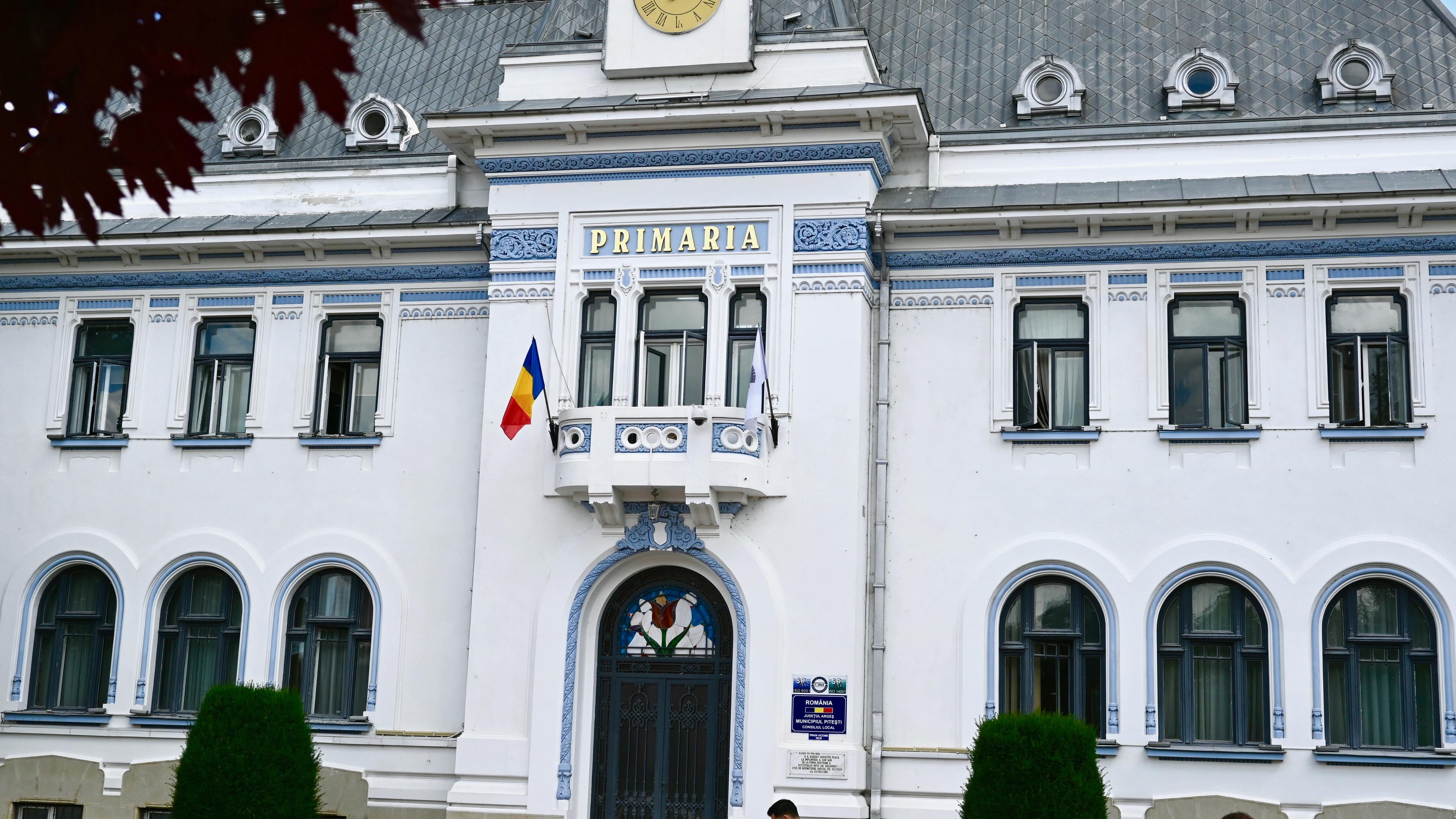 The historical building of the Town Hall in Pitesti. A white old building with the romanian flag and blue details