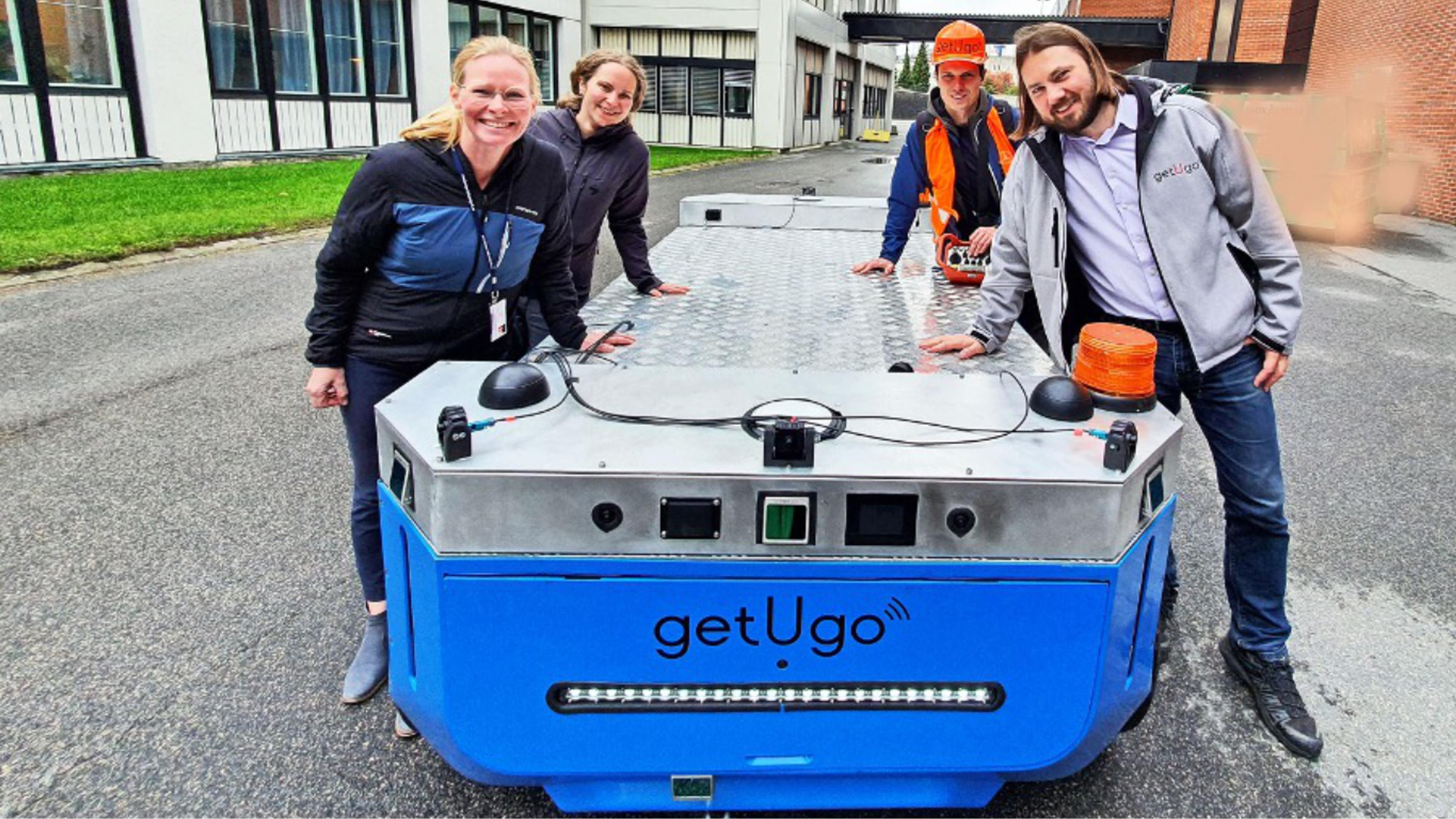 four people standing besides the vehicle, smiling