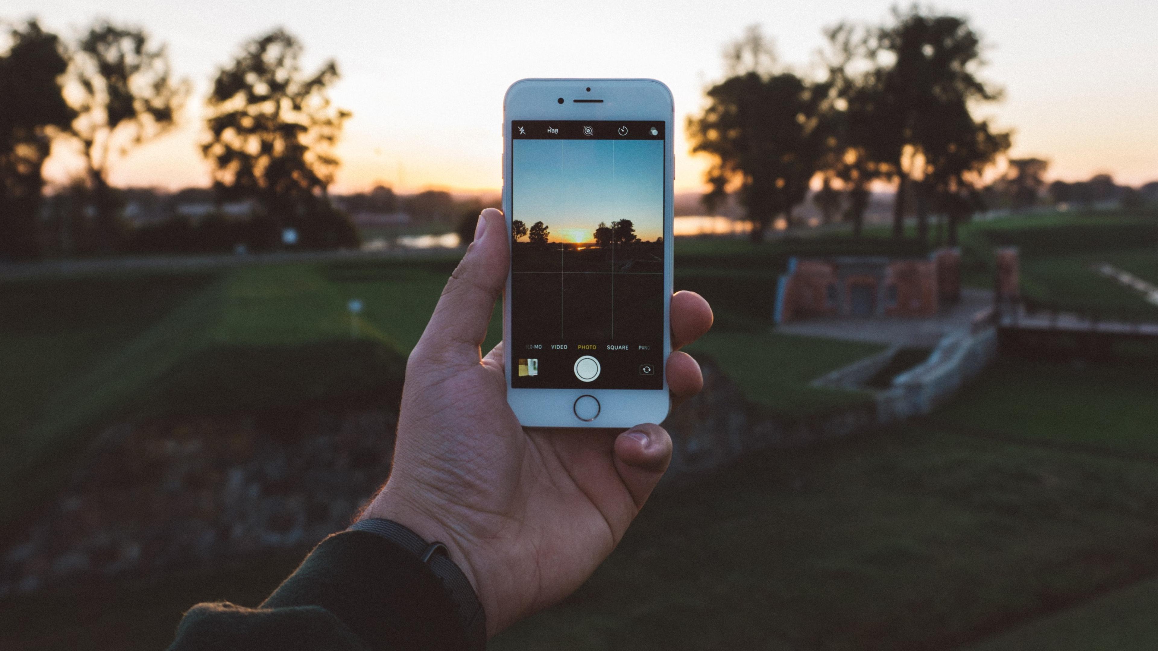 Hand holding a phone taking a photo of the sunset