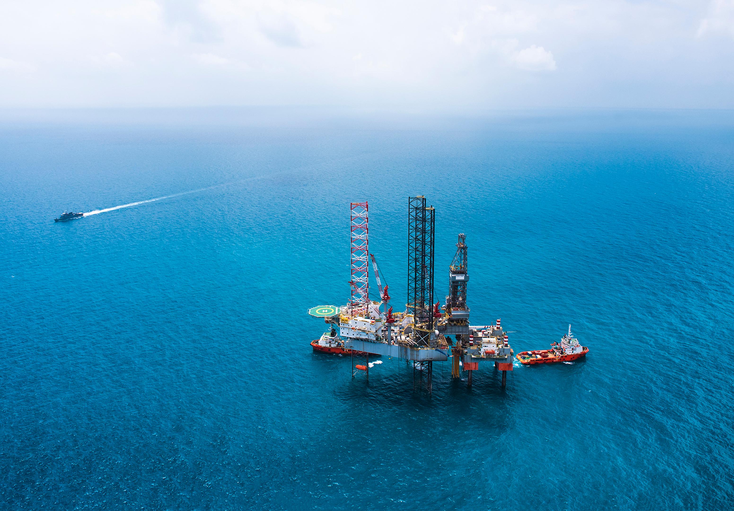 Picture of oil rig at sea with a ship in the background sailing past