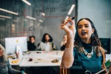 Ung forretningskvinne skriver på glass mens hun forklarer strategi til kolleger i oppstartsselskap