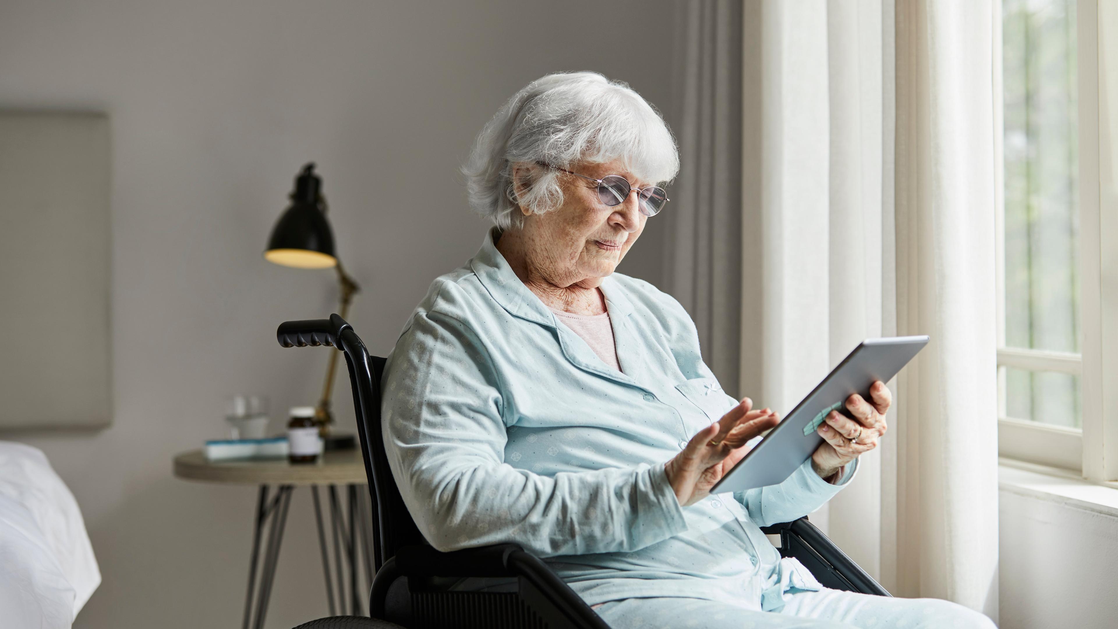 Eldre kvinne i rullestol som bruker tablet