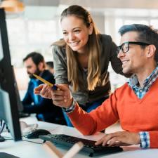 En mann viser noe på pc-skjermen sin til en kvinne som står ved siden av