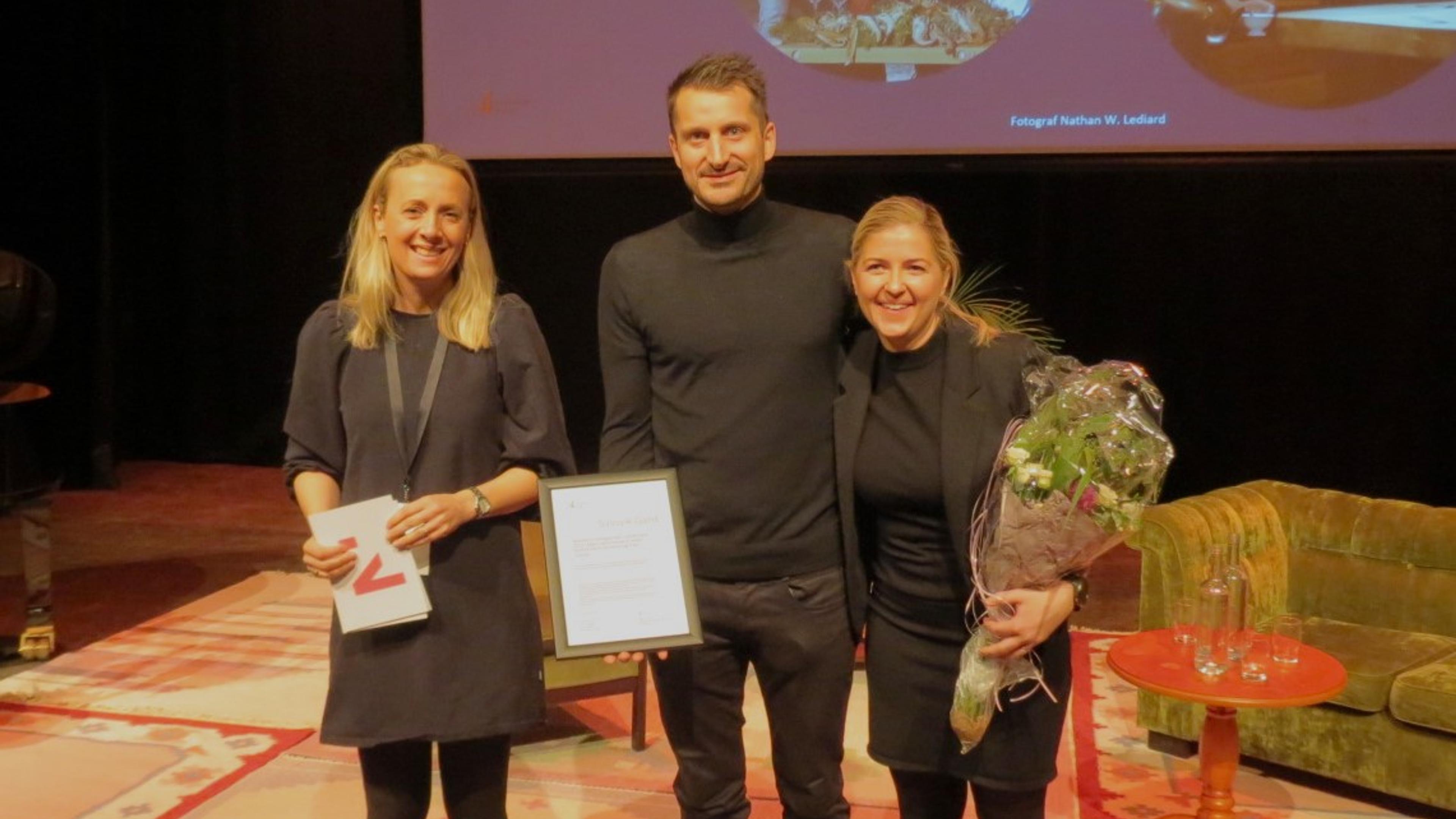 Ei kvinne og en mann mottar diplom og blomster for BU-prisen av ei kvinne med talekort fra Innovasjon Norge i hendene