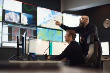 To men ser og peker på en vegg av skjermer foran seg