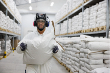 Mann med verneutstyr bærer en sekk inne i et lagerlokale