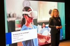 En dame står foran et bilde av helseteknologi og presenterer noe.