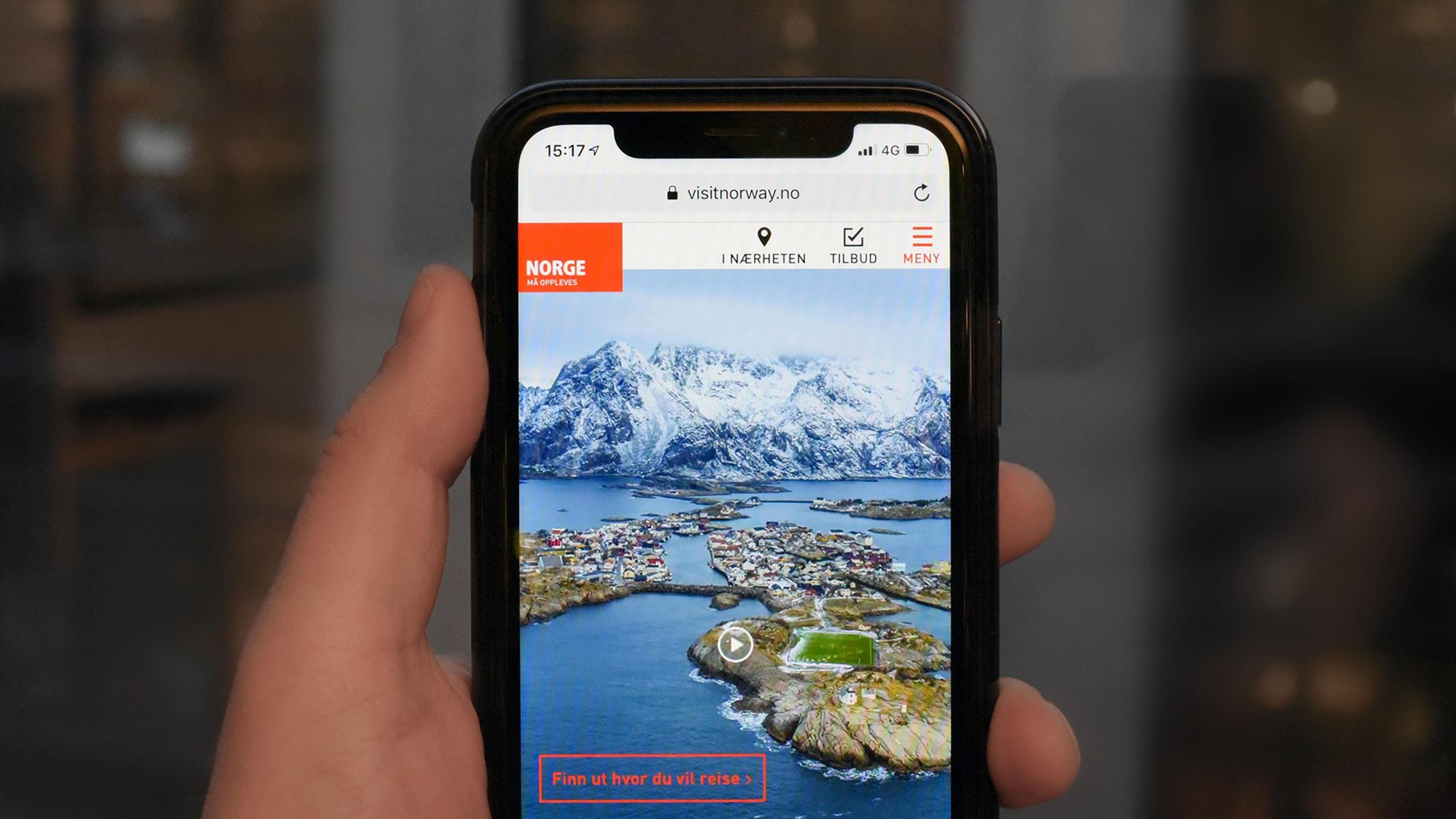 Hånd med mobil som surfer på Visit Norway