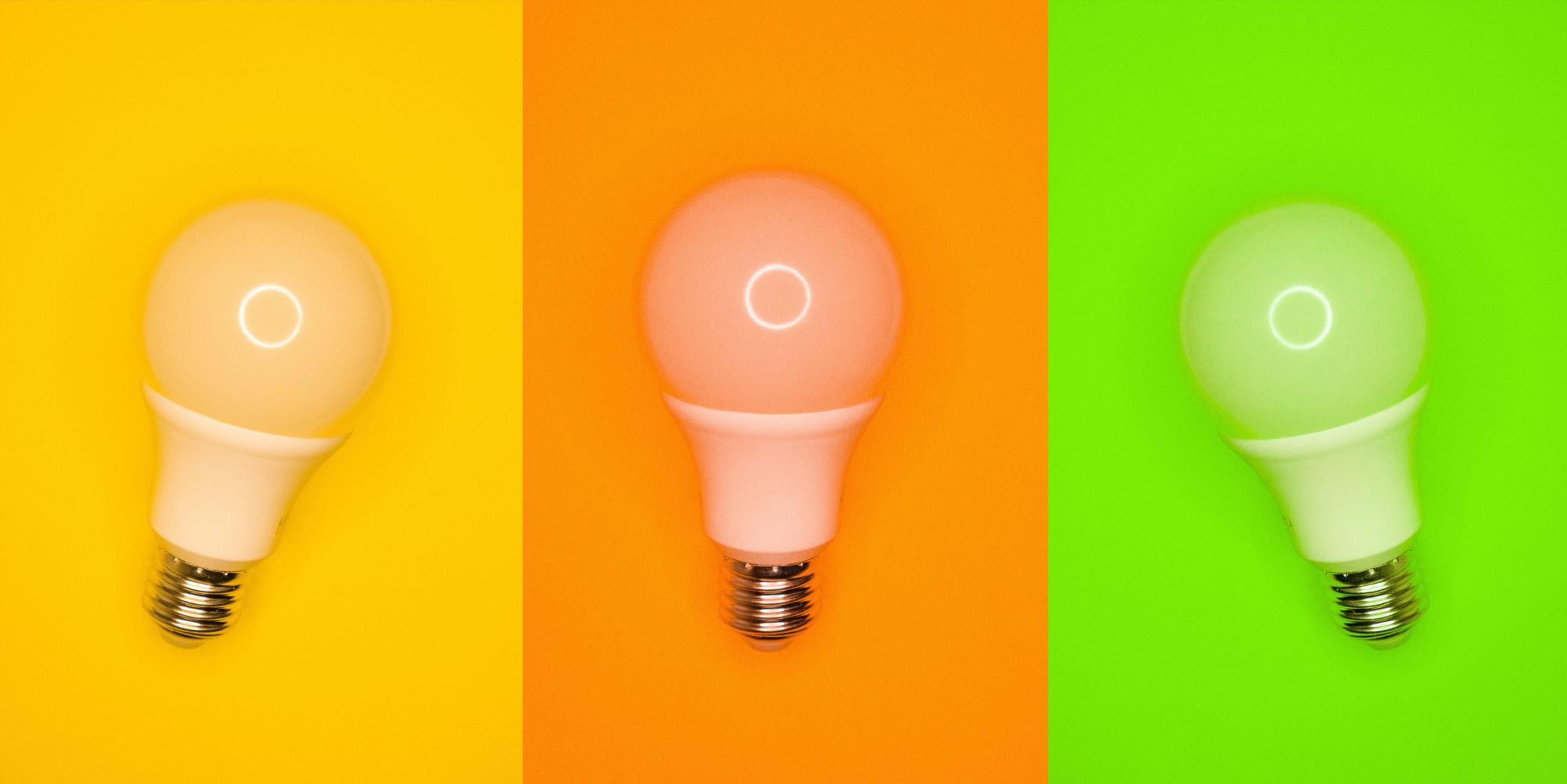 Tre lyspærer ligger ved siden av hverandre med sterke bakgrunnsfarger i gul, oransje og grønn