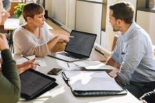 Fem personer i et møte, en av kvinnene peket på en pc-skjerm