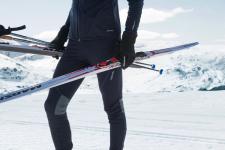 En person holder sine langrennsski og staver ved siden av skiløypa